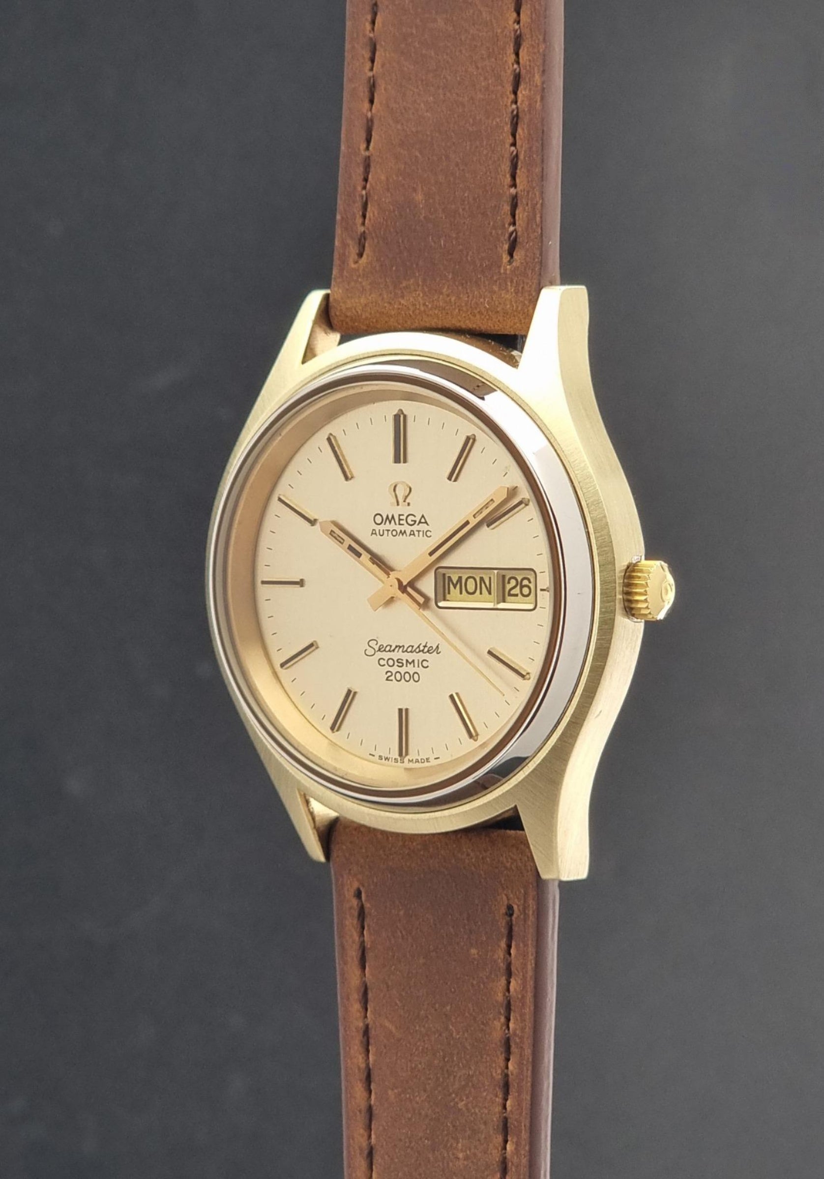 Vintage Omega Wristwatch Seamaster Cosmic 2000 Jumbo 166.129 with a gold-tone case, gold dial, and brown leather strap, shown against a dark gray background.