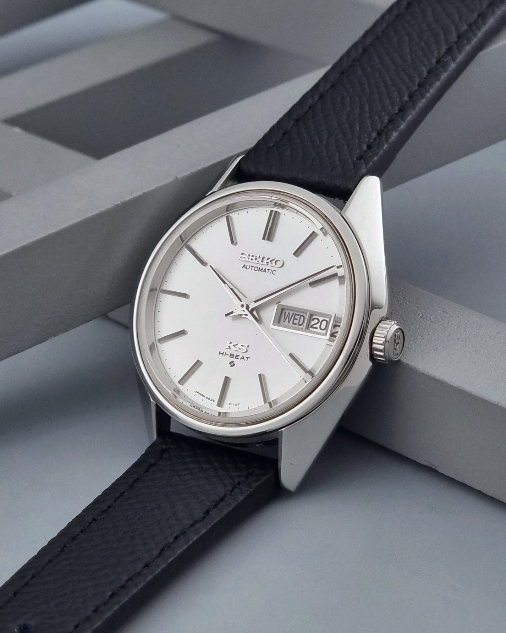 Vintage King Seiko 5626-7110 Wristwatch with a silver case and black strap on a dark gray background crown view