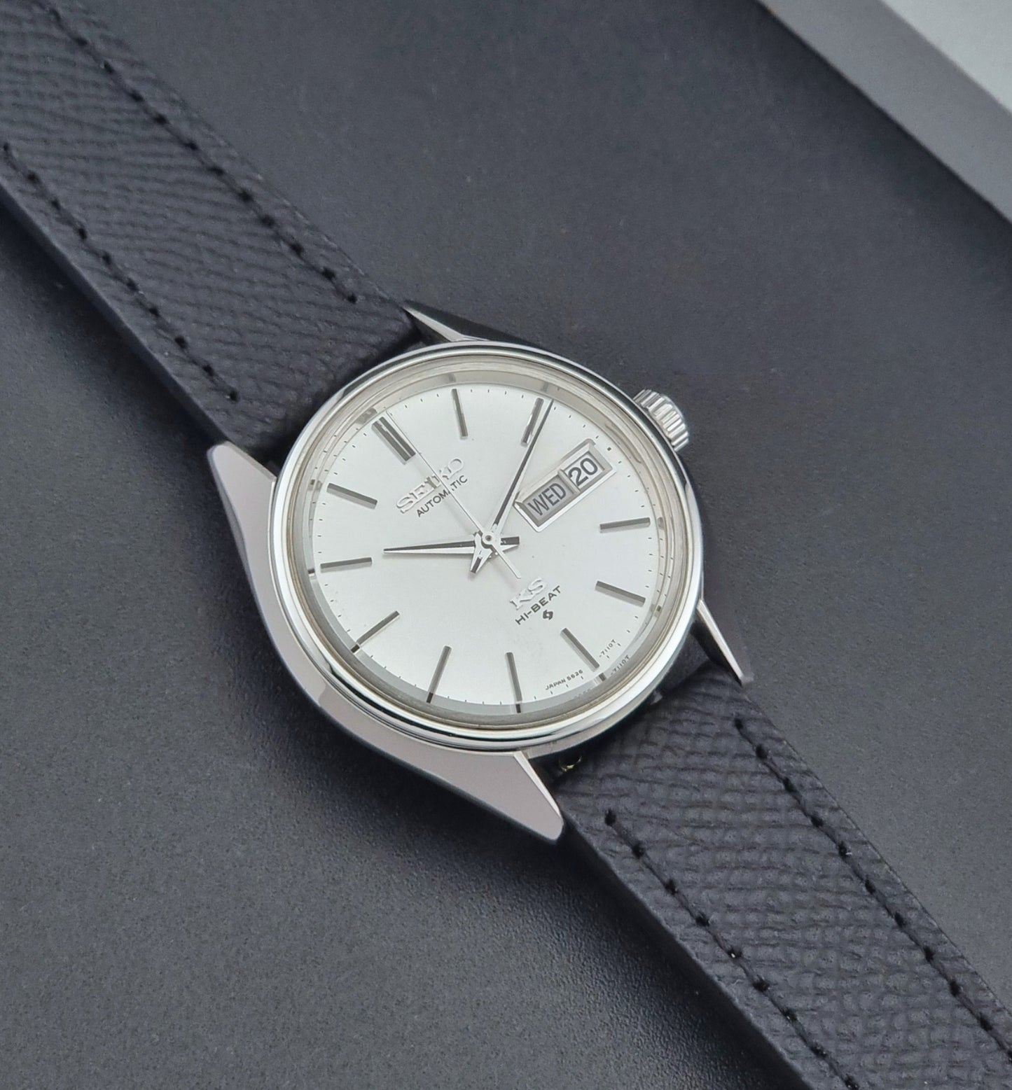 Vintage King Seiko 5626-7110 Wristwatch with a silver case and black strap on a dark gray background close up dial view
