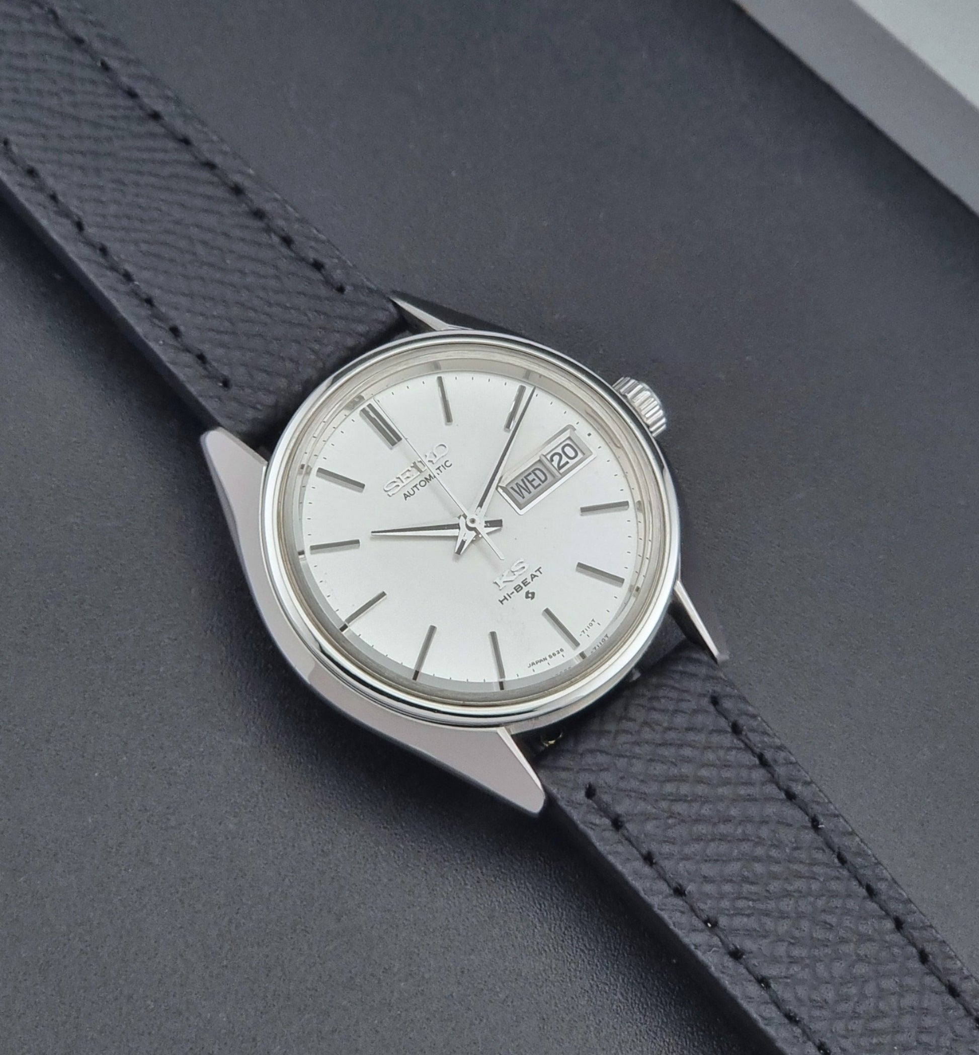 Vintage King Seiko 5626-7110 Wristwatch with a silver case and black strap on a dark gray background close up dial view
