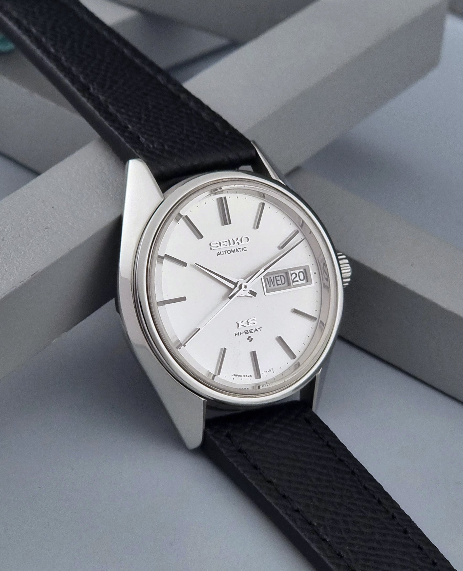 Vintage King Seiko 5626-7110 Wristwatch with a silver case and black strap on a dark gray background side view