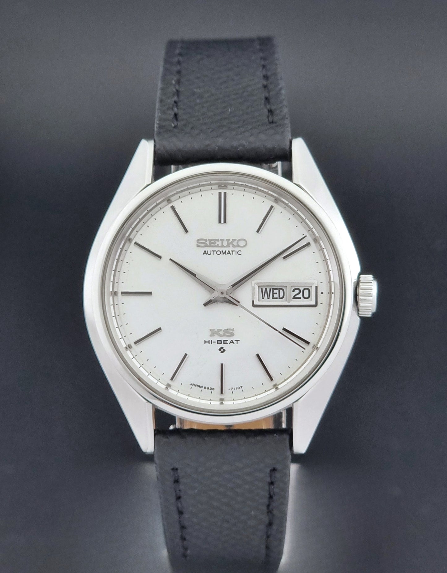 Vintage King Seiko 5626-7110 Wristwatch with a silver case and black strap on a dark gray background close dial view