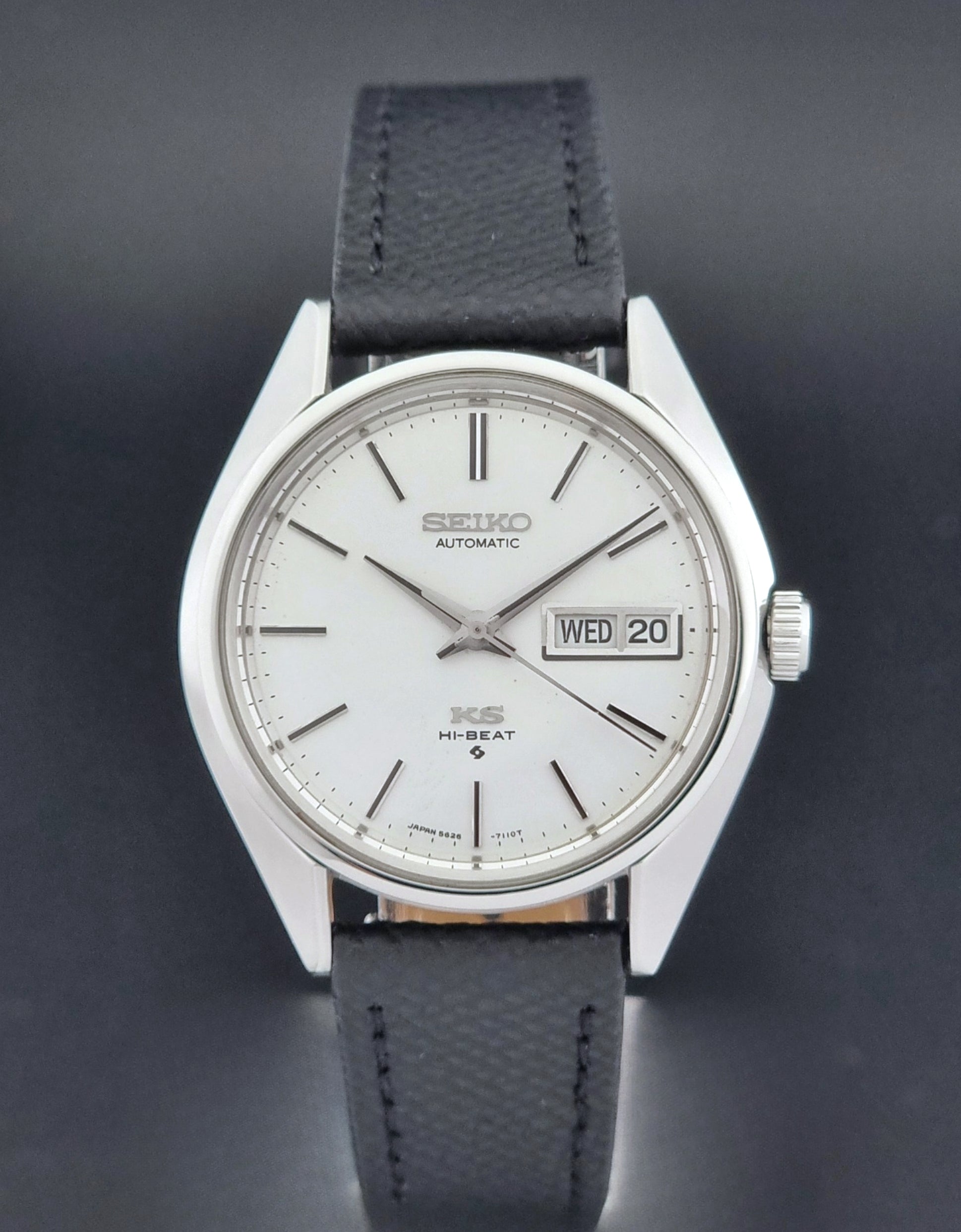Vintage King Seiko 5626-7110 Wristwatch with a silver case and black strap on a dark gray background close dial view