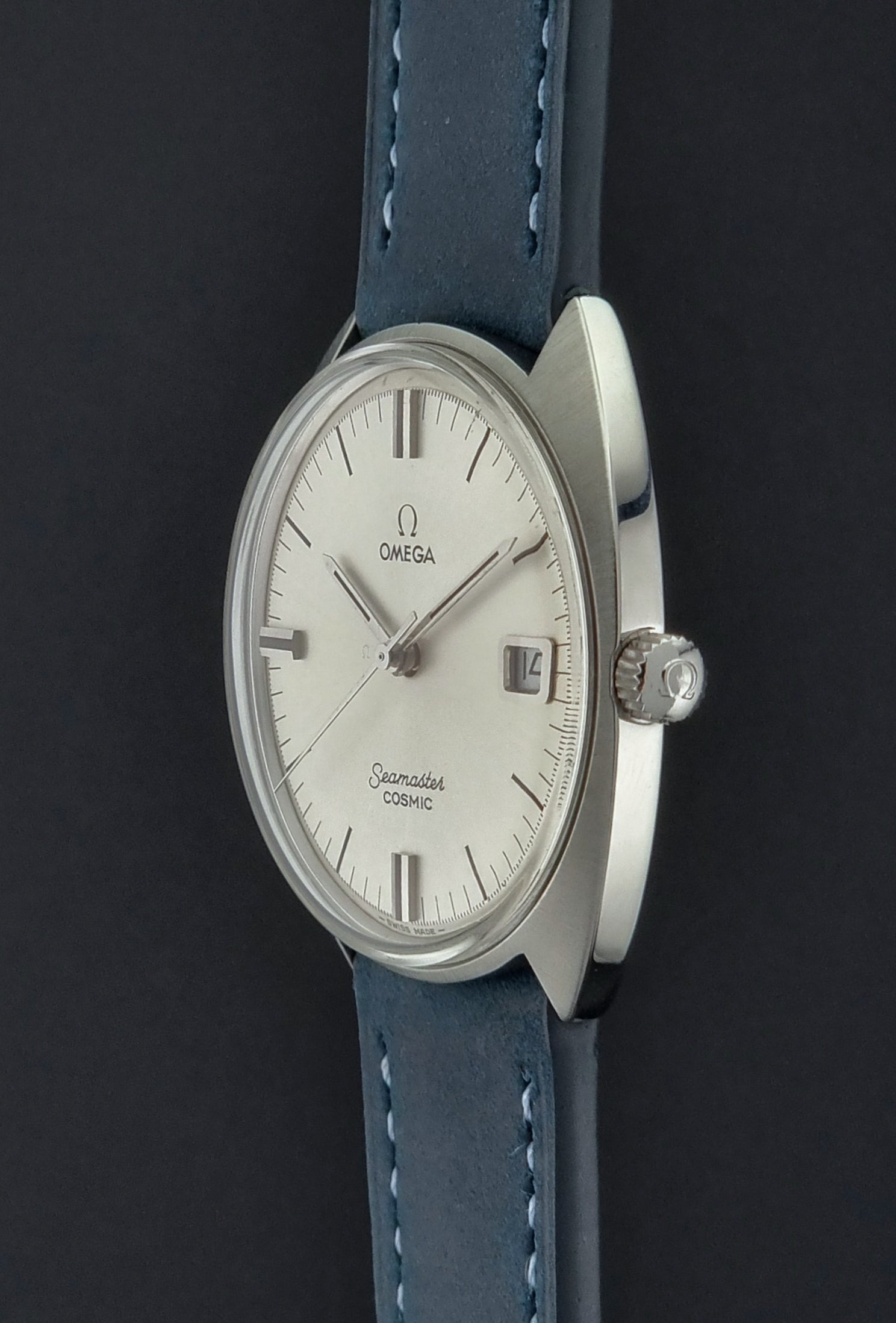 Vintage Omega Seamaster Cosmic wristwatch with blue strap and silver case on a gray background crown view