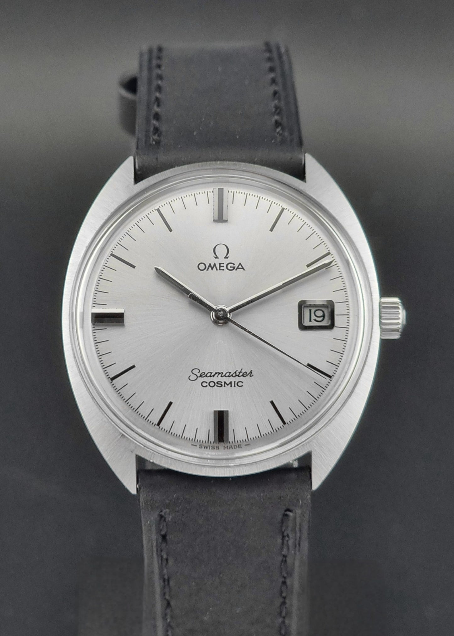 Omega Seamaster Cosmic 136.017 watch with silver dial and black leather strap on a dark background 