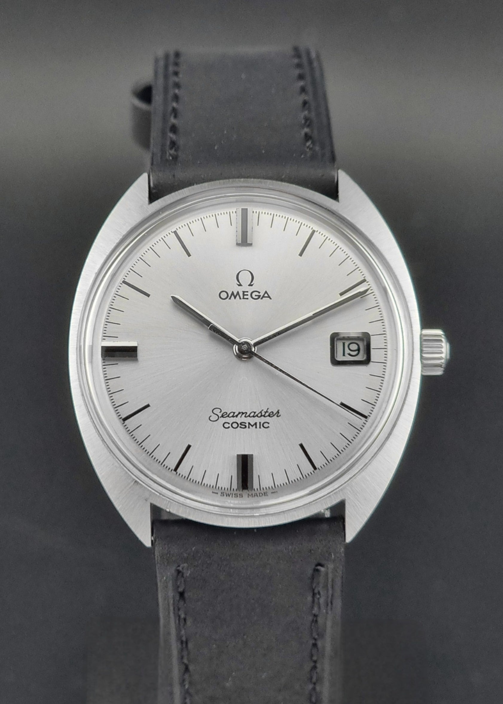 Omega Seamaster Cosmic 136.017 watch with silver dial and black leather strap on a dark background 