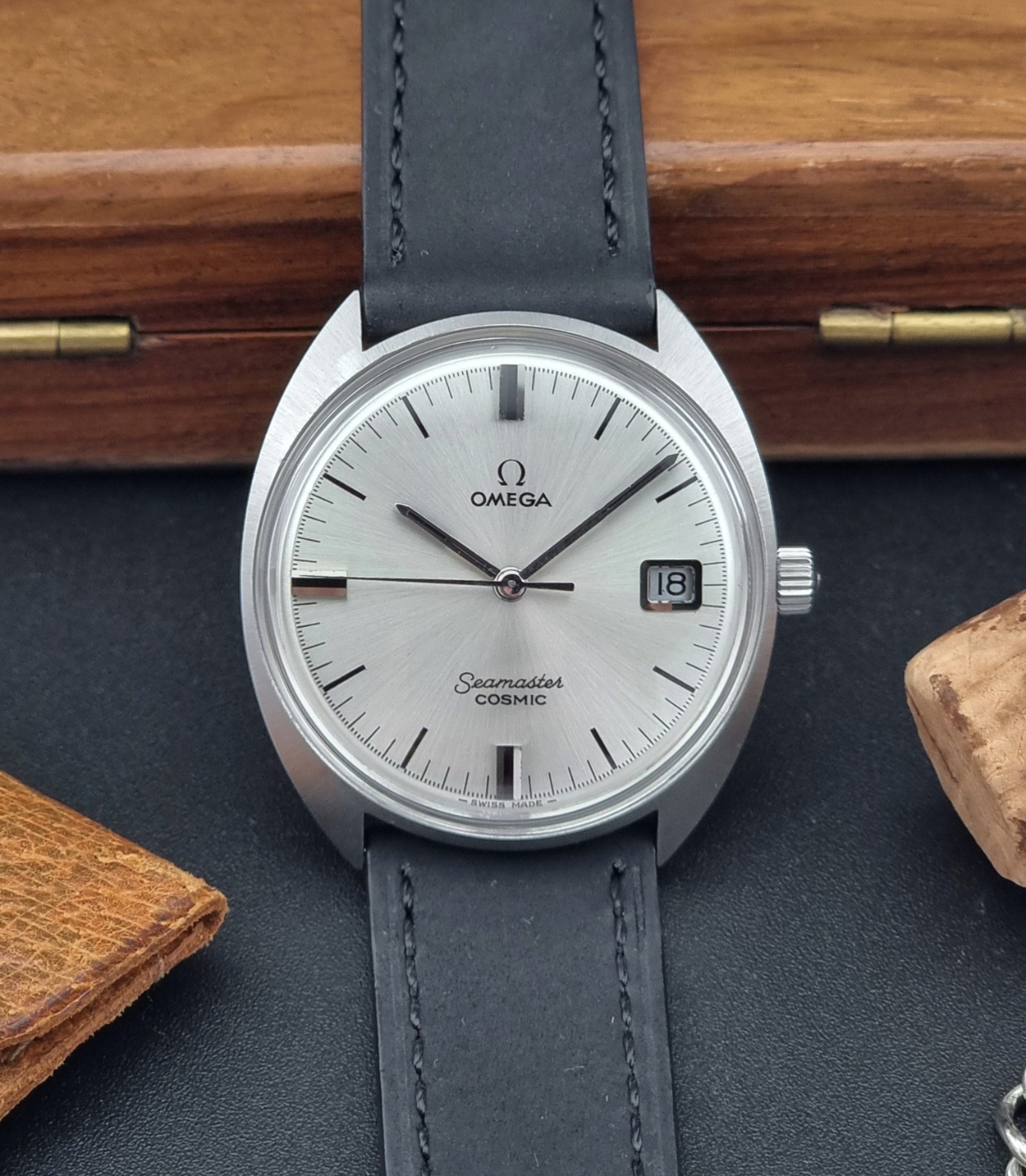 Omega Seamaster Cosmic 136.017  watch with gray leather strap on a dark surface with wooden background