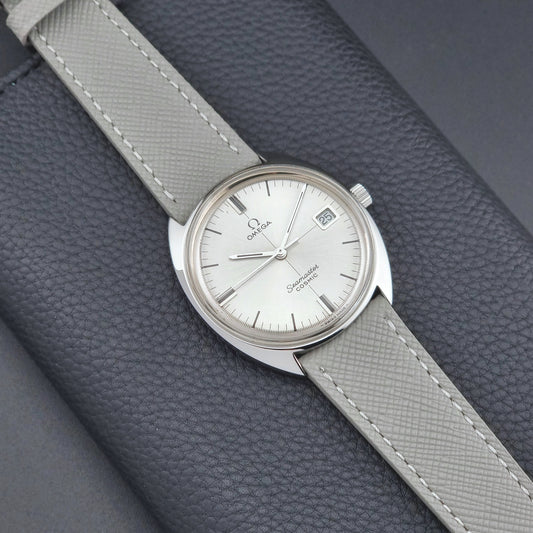 Vintage Omega Seamaster Cosmic watch with gray leather strap on a textured gray background