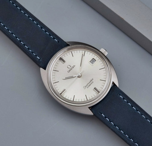 Vintage Omega Seamaster Cosmic wristwatch with blue strap and silver case on a gray background front view 