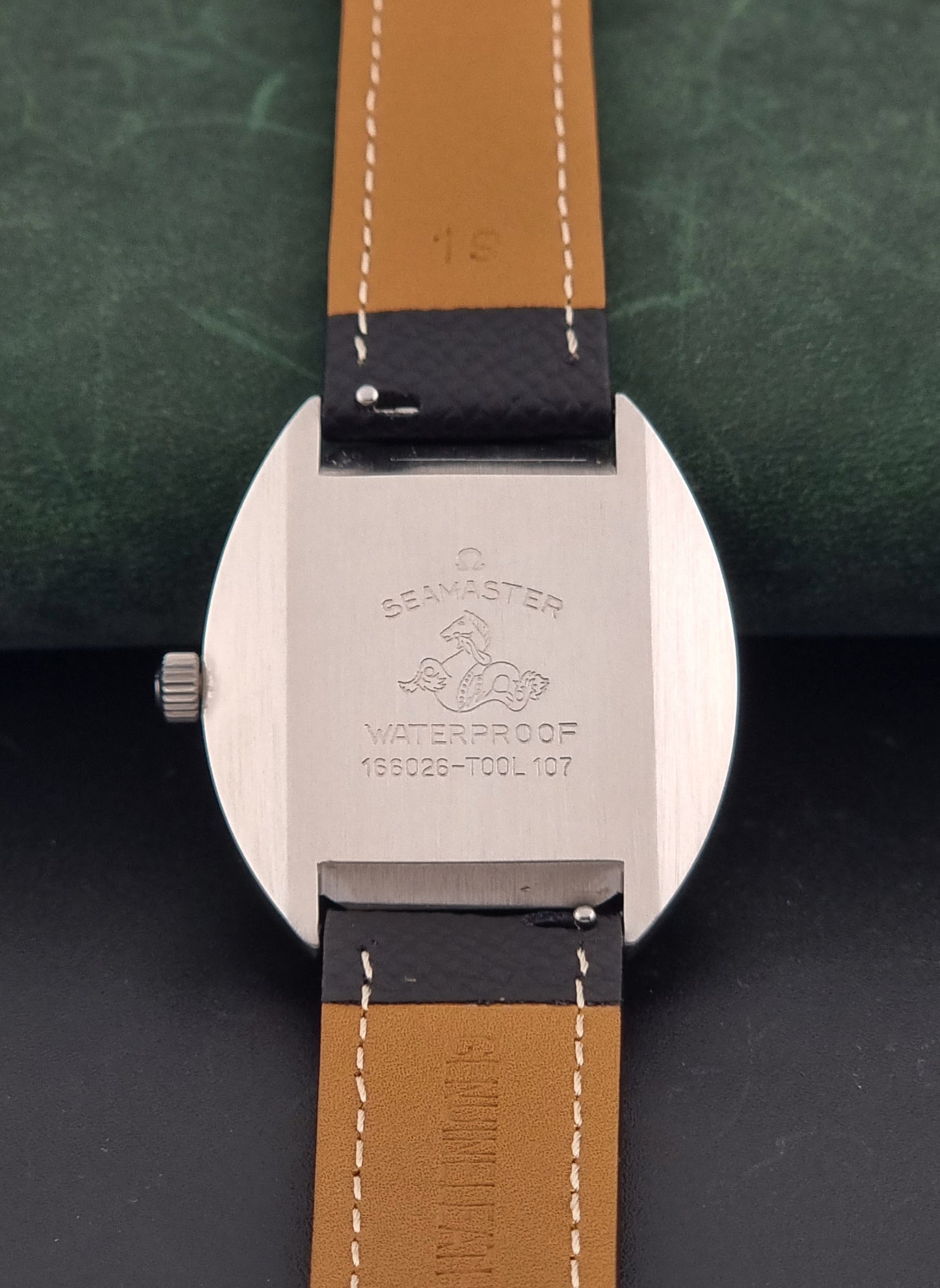 Vintage Omega 166.026 Seamaster Cosmic Automatic watch with a silver-tone case, silver dial, and textured black leather strap, on a dark background case back view