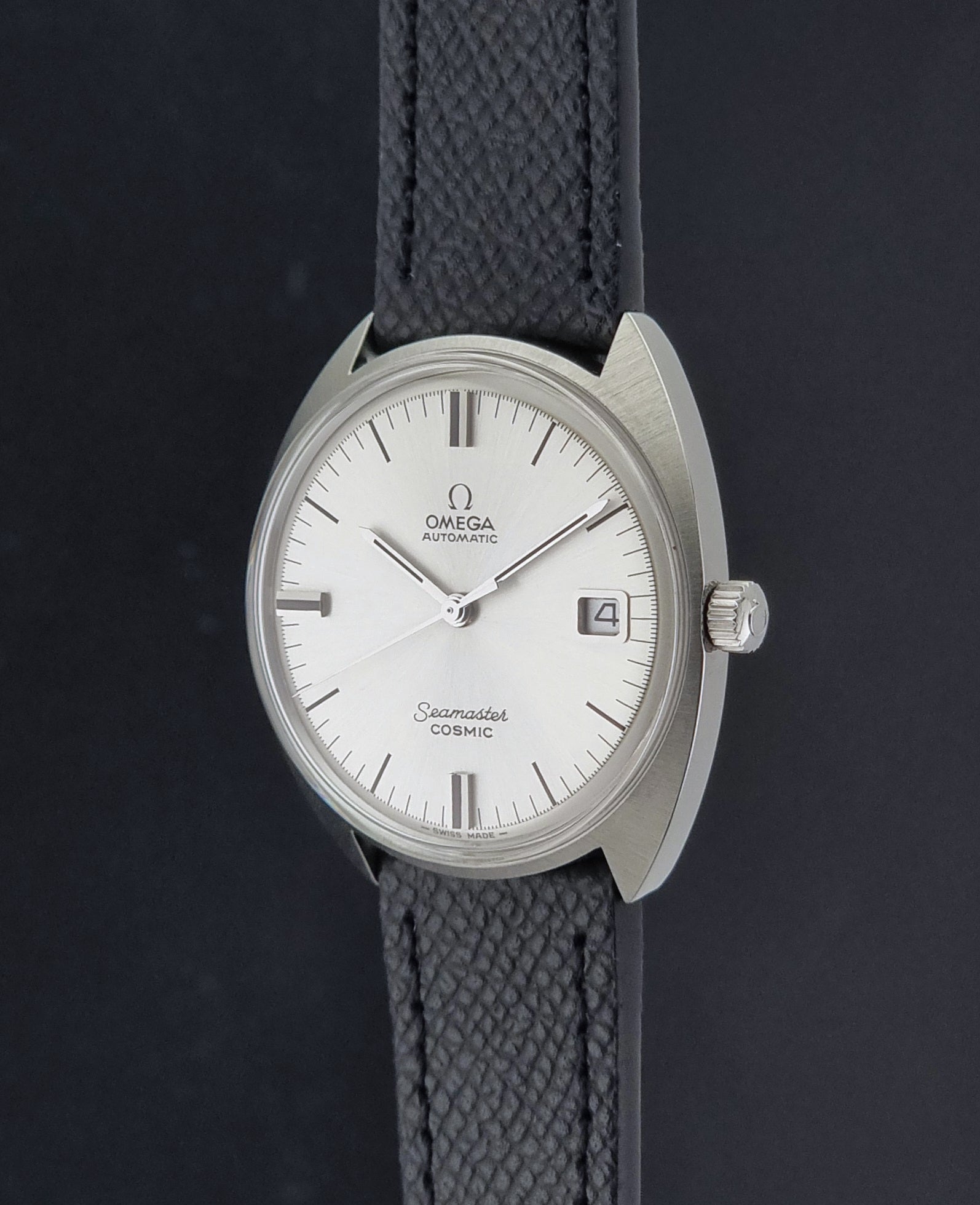 Vintage Omega 166.026 Seamaster Cosmic Automatic watch with a silver-tone case, silver dial, and textured black leather strap, on a dark background crown profile view