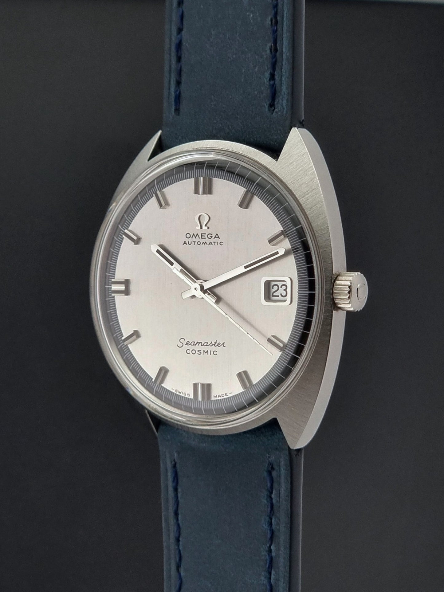 Vintage Omega Wristwatch 166.026 Seamaster Cosmic with blue leather strap on a dark surface with blue strap and silver case on a gray background close crown view