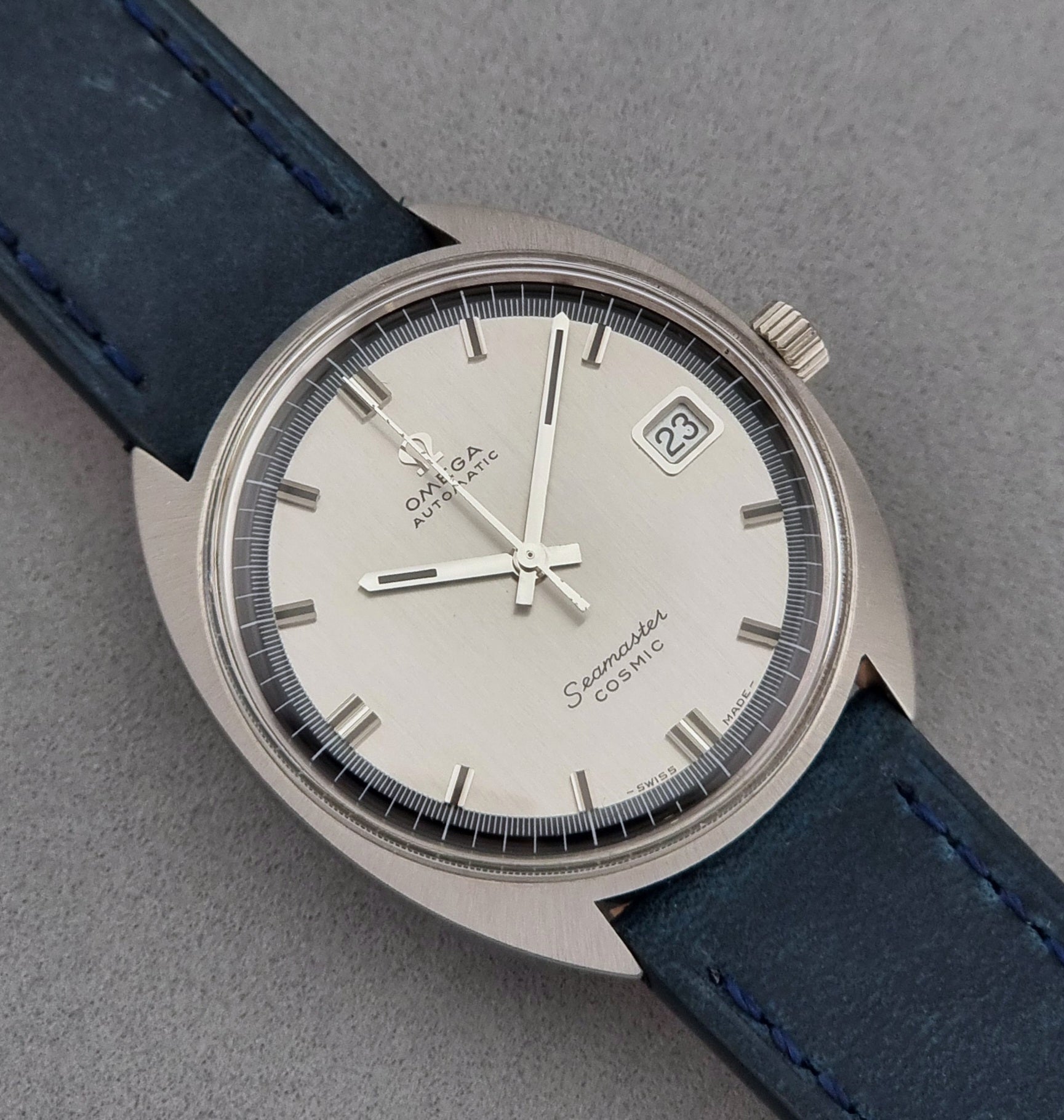 Vintage Omega Wristwatch 166.026 Seamaster Cosmic with blue leather strap on a dark surface with blue strap and silver case on a gray background close dial view