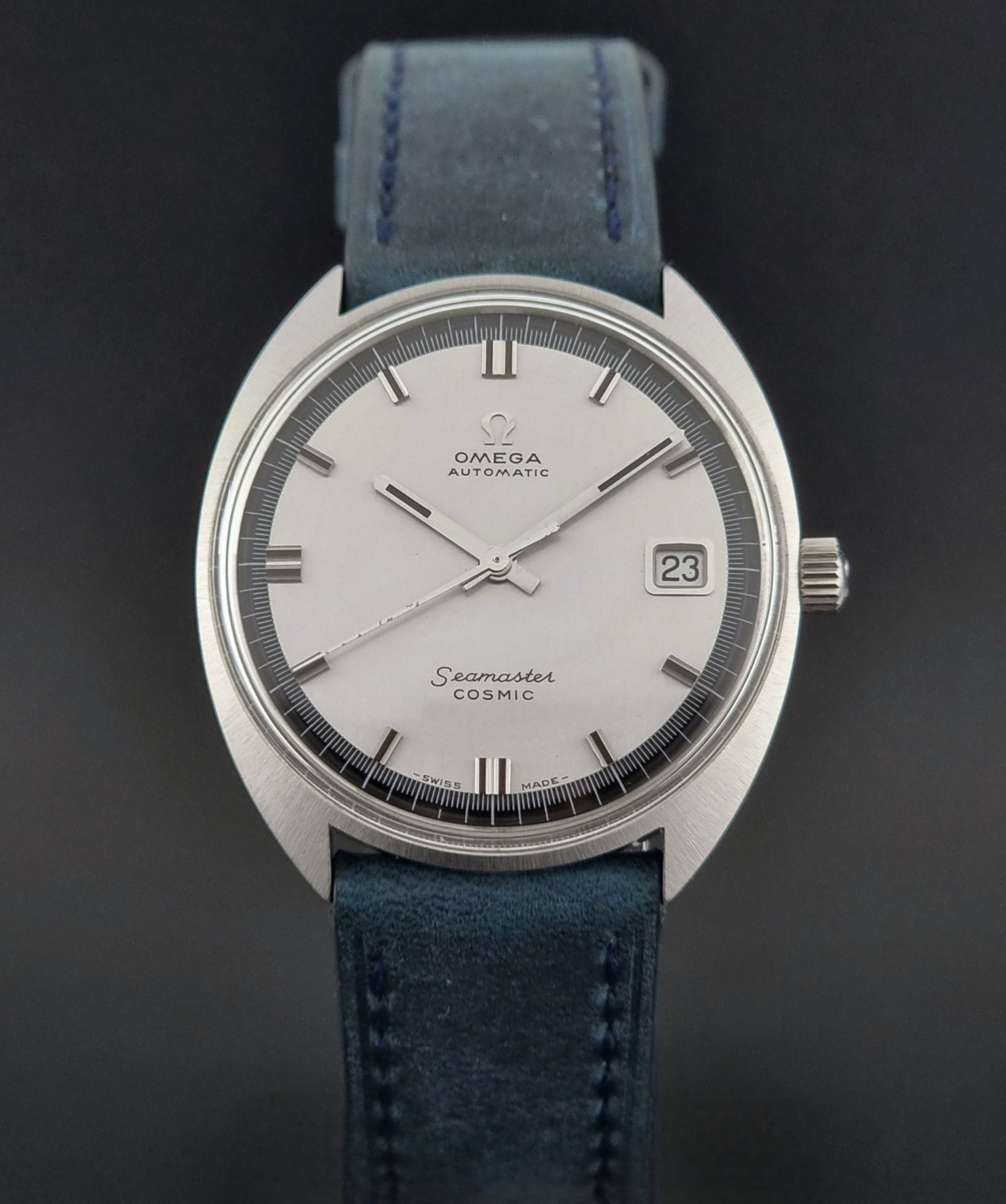 Vintage Omega Wristwatch 166.026 Seamaster Cosmic with blue leather strap on a dark surface with blue strap and silver case on a gray background dial view