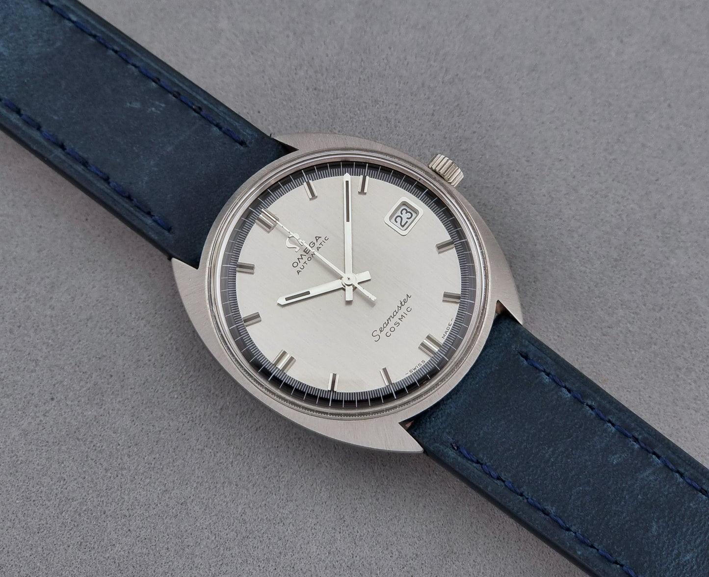 Vintage Omega Wristwatch 166.026 Seamaster Cosmic with blue leather strap on a dark surface with blue strap and silver case on a gray background front