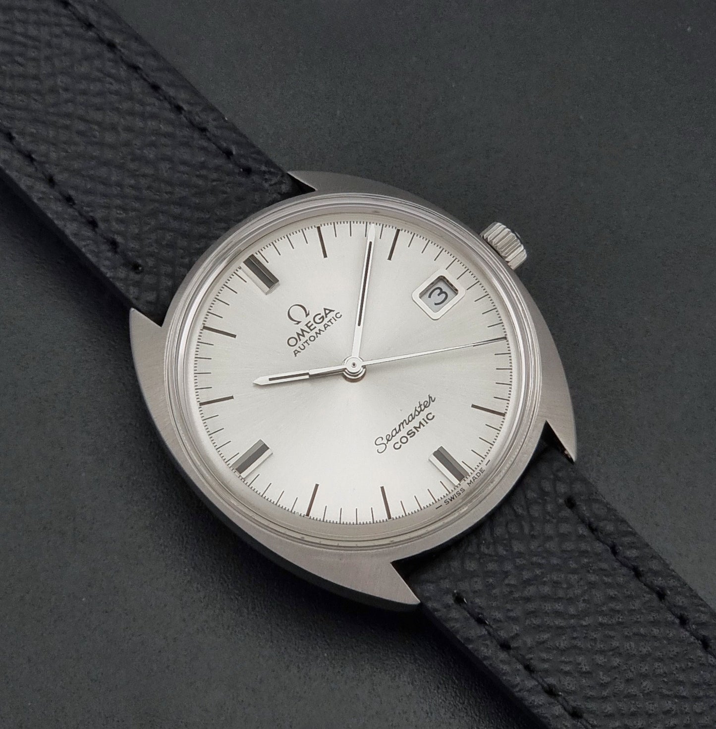 Vintage Omega 166.026 Seamaster Cosmic Automatic watch with a silver-tone case, silver dial, and textured black leather strap, on a dark background close up dial view