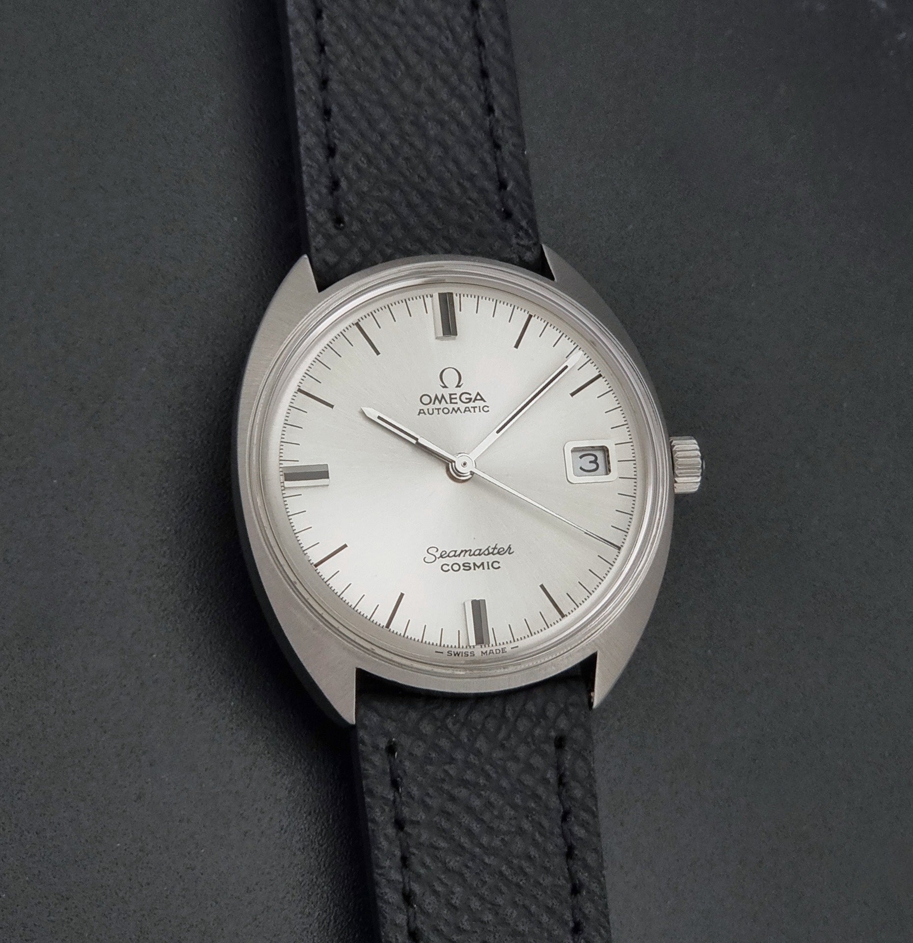 Vintage Omega 166.026 Seamaster Cosmic Automatic watch with a silver-tone case, silver dial, and textured black leather strap, on a dark background front view
