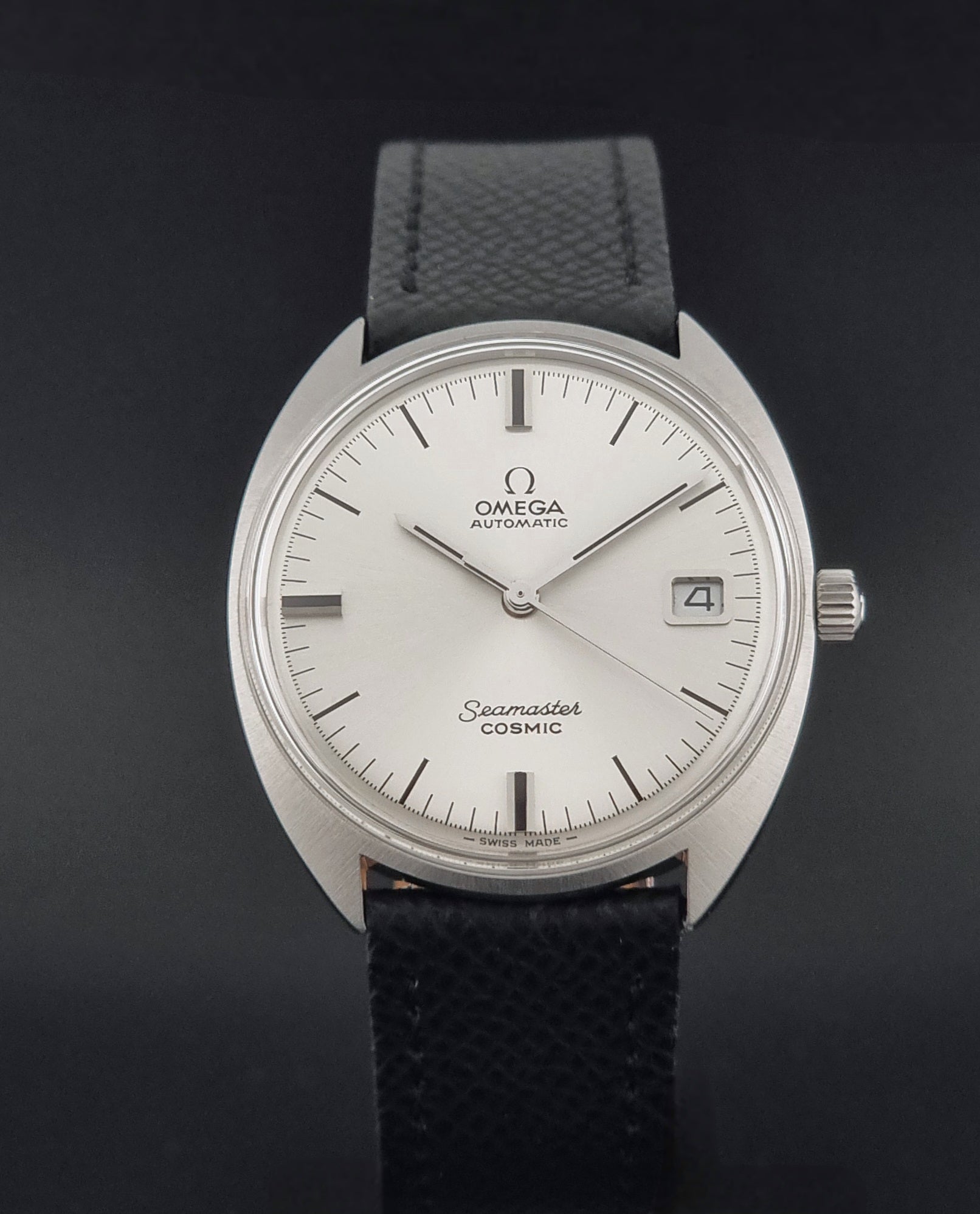 Vintage Omega 166.026 Seamaster Cosmic Automatic watch with a silver-tone case, silver dial, and textured black leather strap, on a dark background close dial view