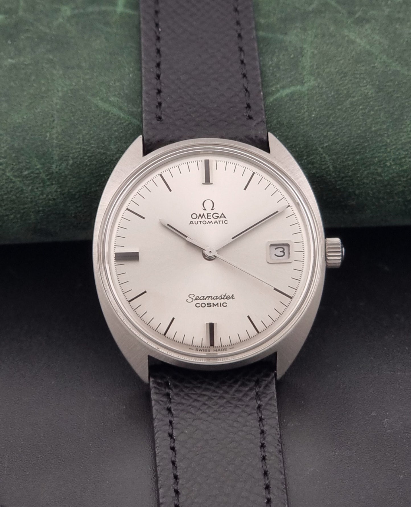 Vintage Omega 166.026 Seamaster Cosmic Automatic watch with a silver-tone case, silver dial, and textured black leather strap, on a dark background dial view