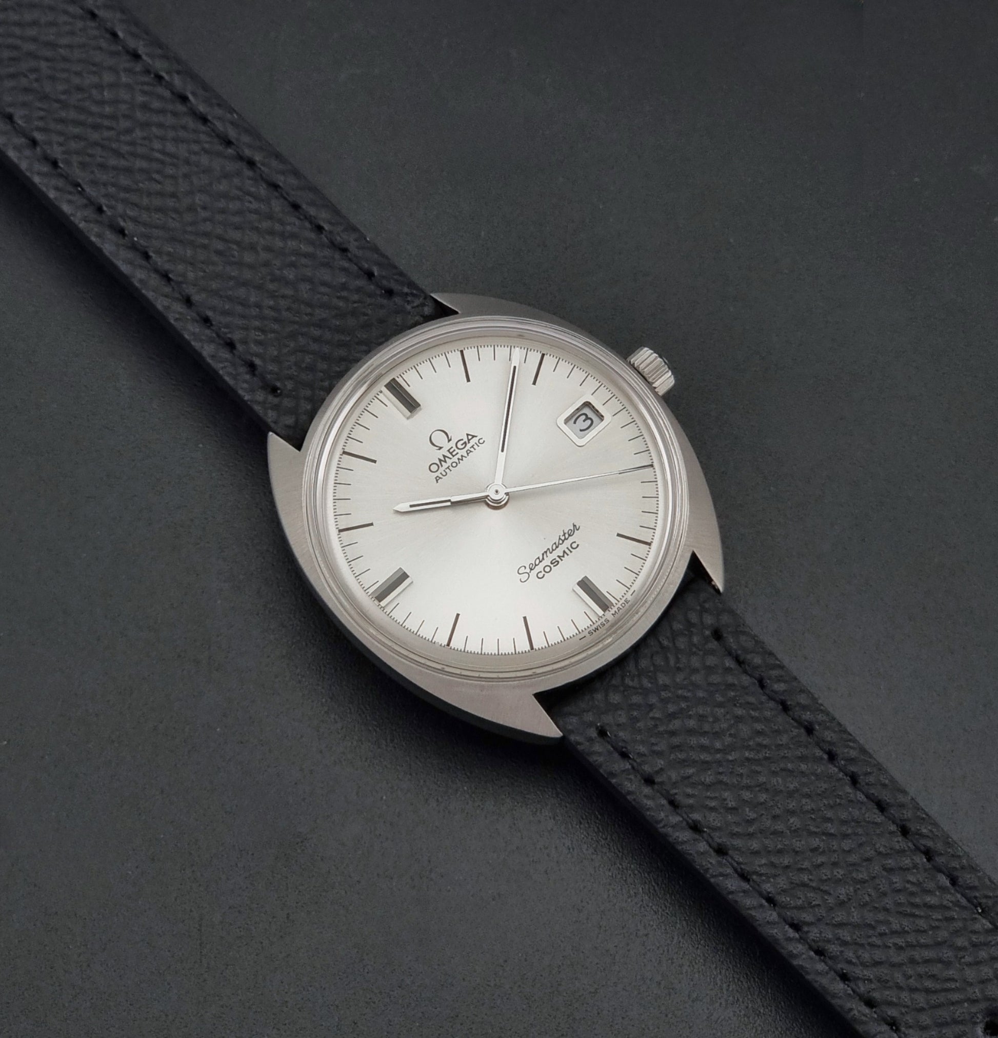 Vintage Omega 166.026 Seamaster Cosmic Automatic watch with a silver-tone case, silver dial, and textured black leather strap, on a dark background dial