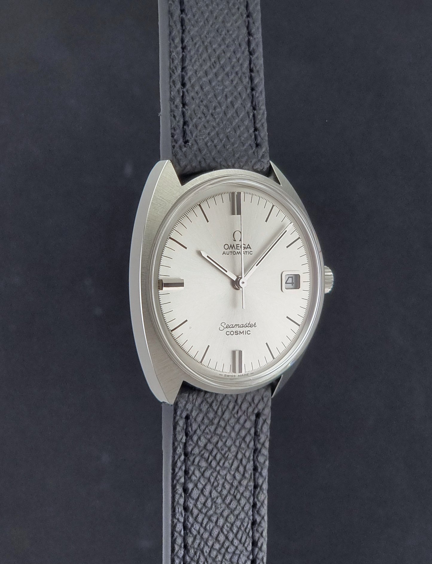 Vintage Omega 166.026 Seamaster Cosmic Automatic watch with a silver-tone case, silver dial, and textured black leather strap, on a dark background side profile view