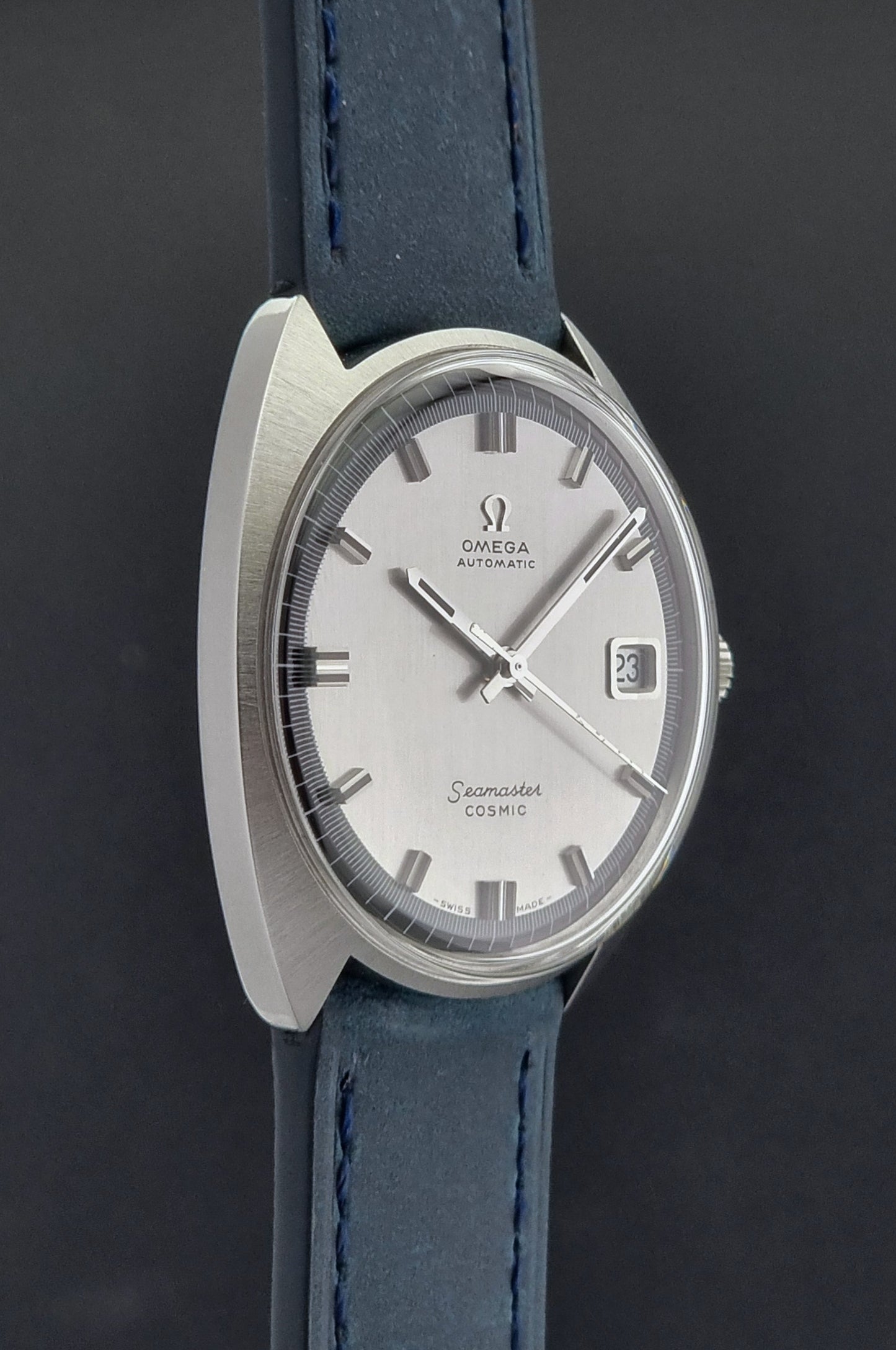 Vintage Omega Wristwatch 166.026 Seamaster Cosmic with blue leather strap on a dark surface with blue strap and silver case on a gray background side profile view