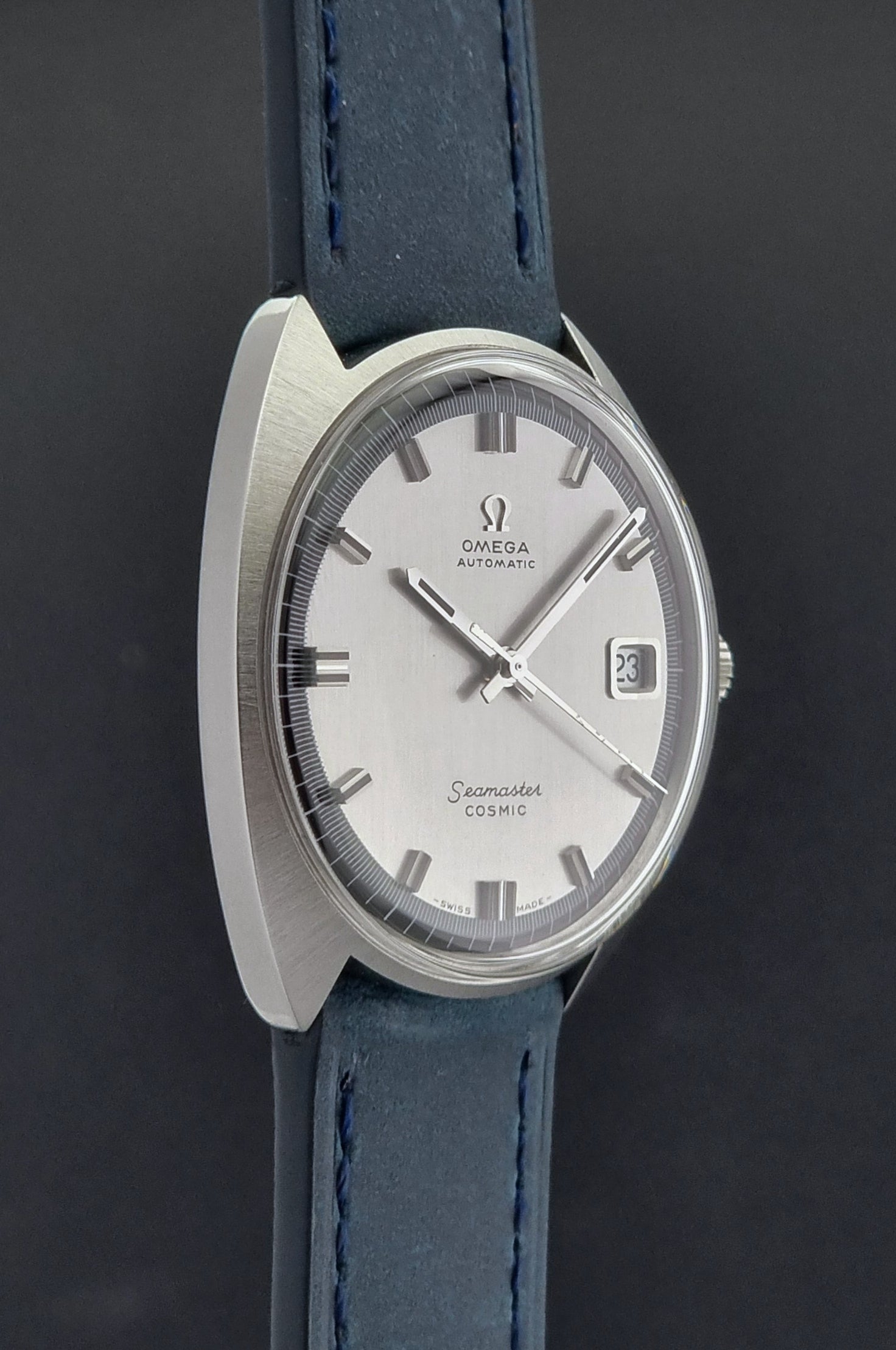 Vintage Omega Wristwatch 166.026 Seamaster Cosmic with blue leather strap on a dark surface with blue strap and silver case on a gray background side profile view