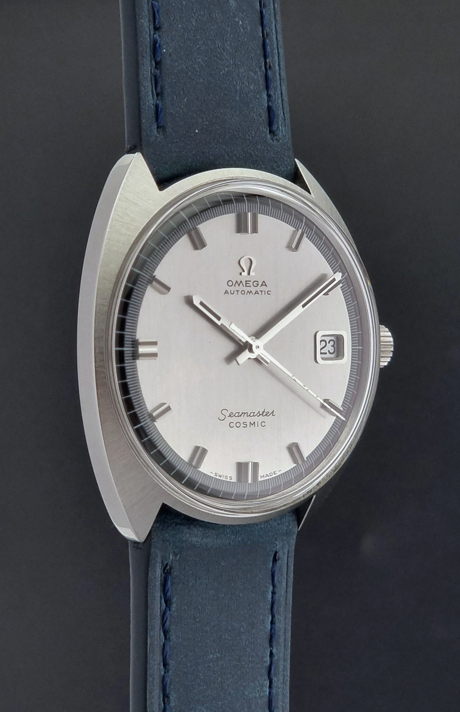 Vintage Omega Wristwatch 166.026 Seamaster Cosmic with blue leather strap on a dark surface with blue strap and silver case on a gray background close side profile
