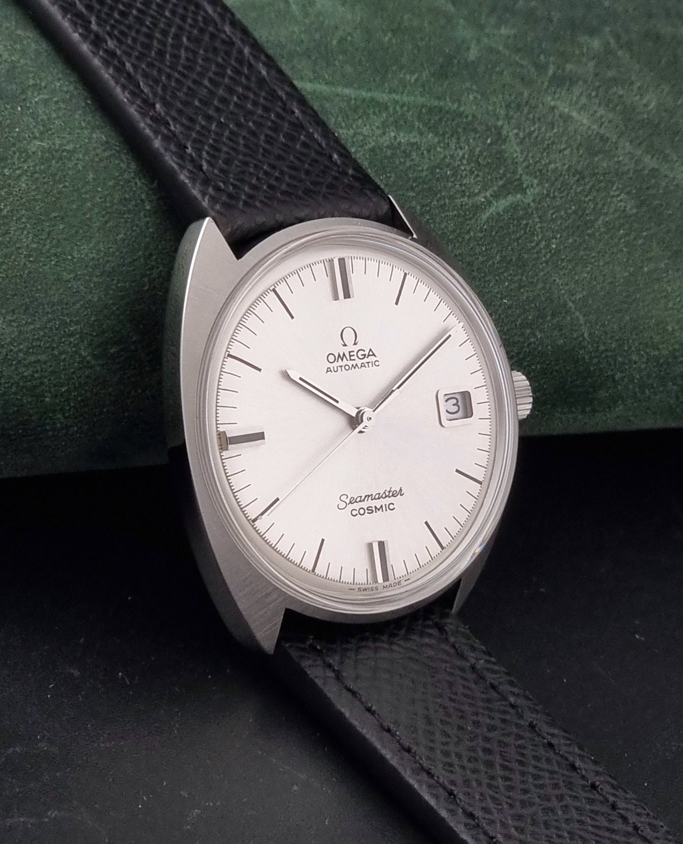 Vintage Omega 166.026 Seamaster Cosmic Automatic watch with a silver-tone case, silver dial, and textured black leather strap, on a dark background side view