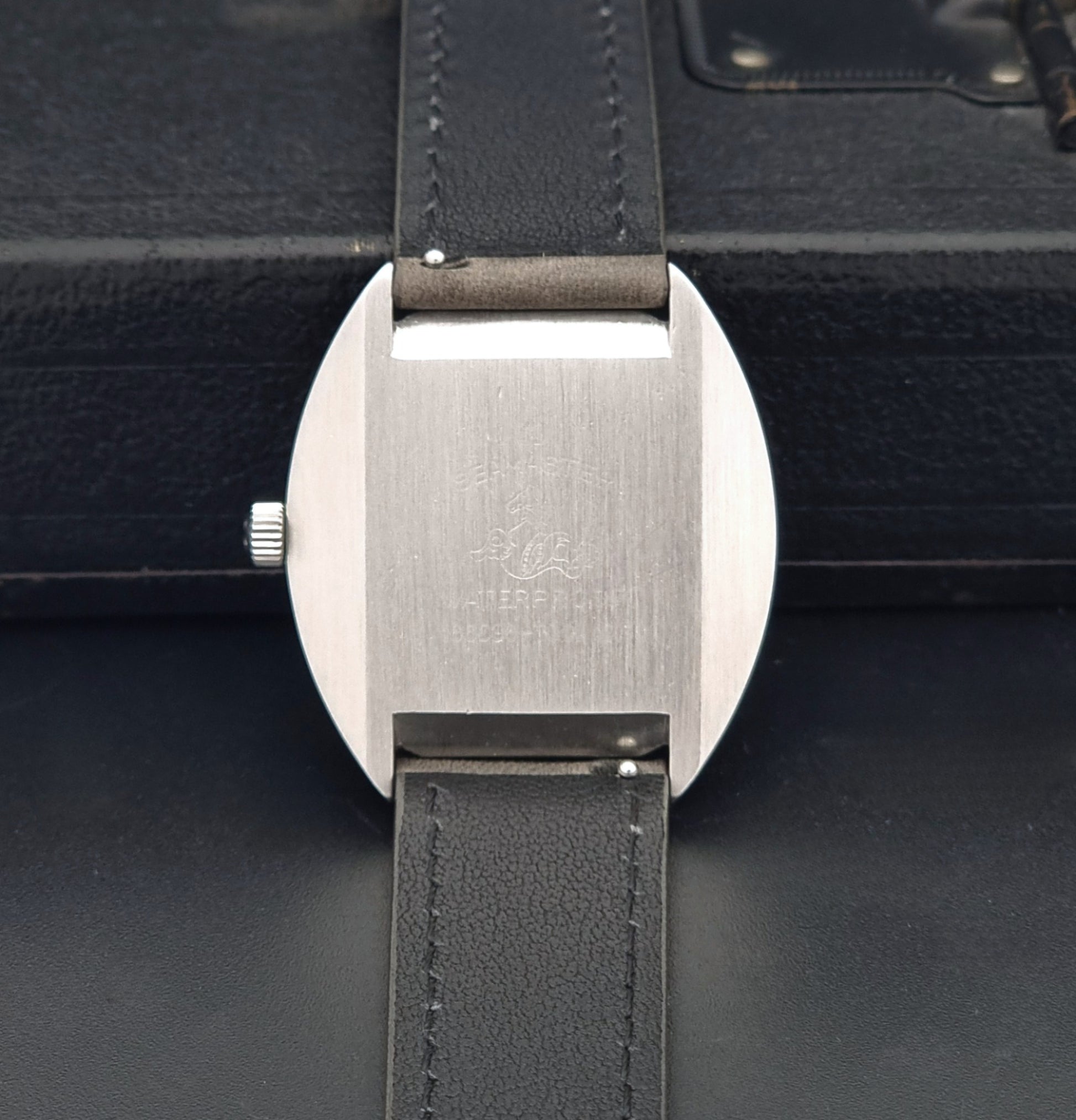 Vintage Omega 166.036 Seamaster Cosmic watch with a silver-toned case, a light gray dial with a day-date window, and a gray leather strap, on a dark background case back view