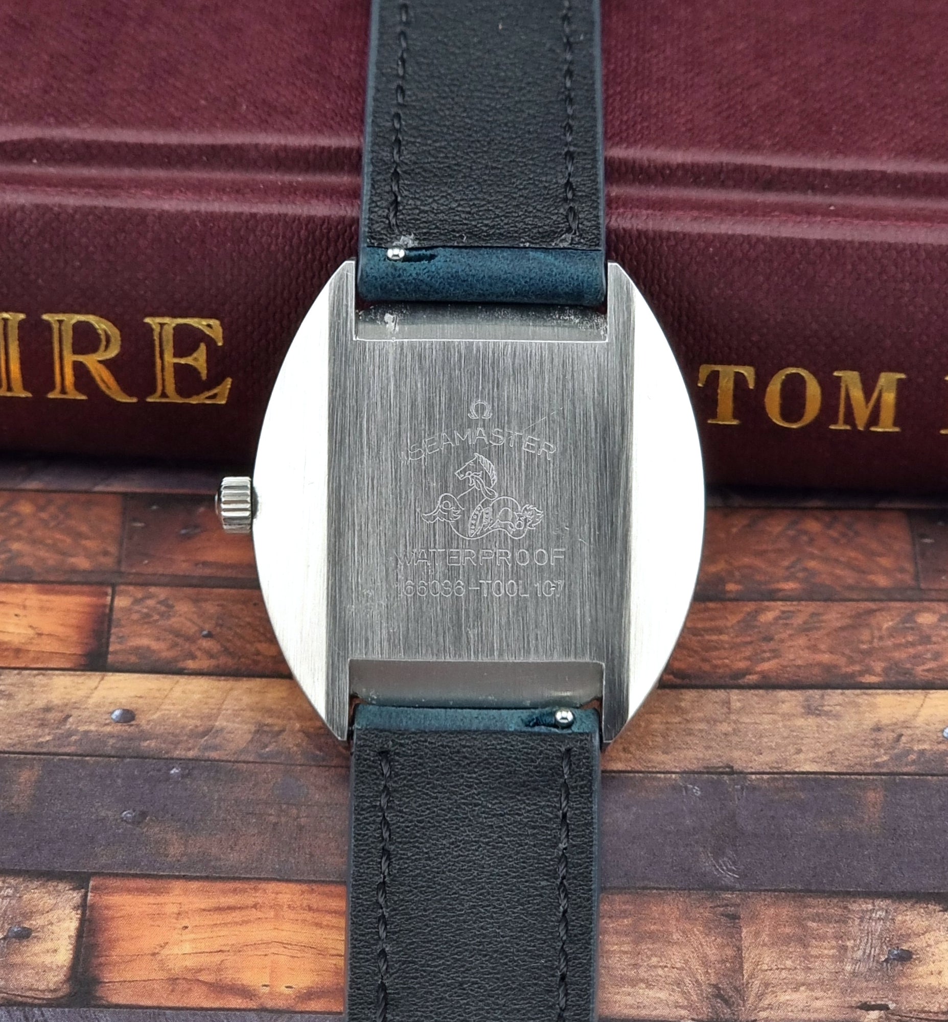 Vintage Omega Seamaster Cosmic Close-up of the watch case back with a black leather strap on a wooden surface