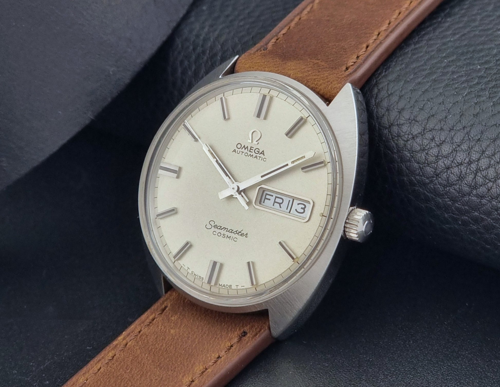 Vintage Omega Seamaster Cosmic 166.036 wristwatch with brown leather strap on a dark background crown view