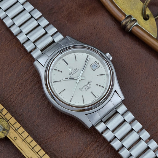 Silver Omega Seamaster watch on a brown leather surface with a key and ruler.