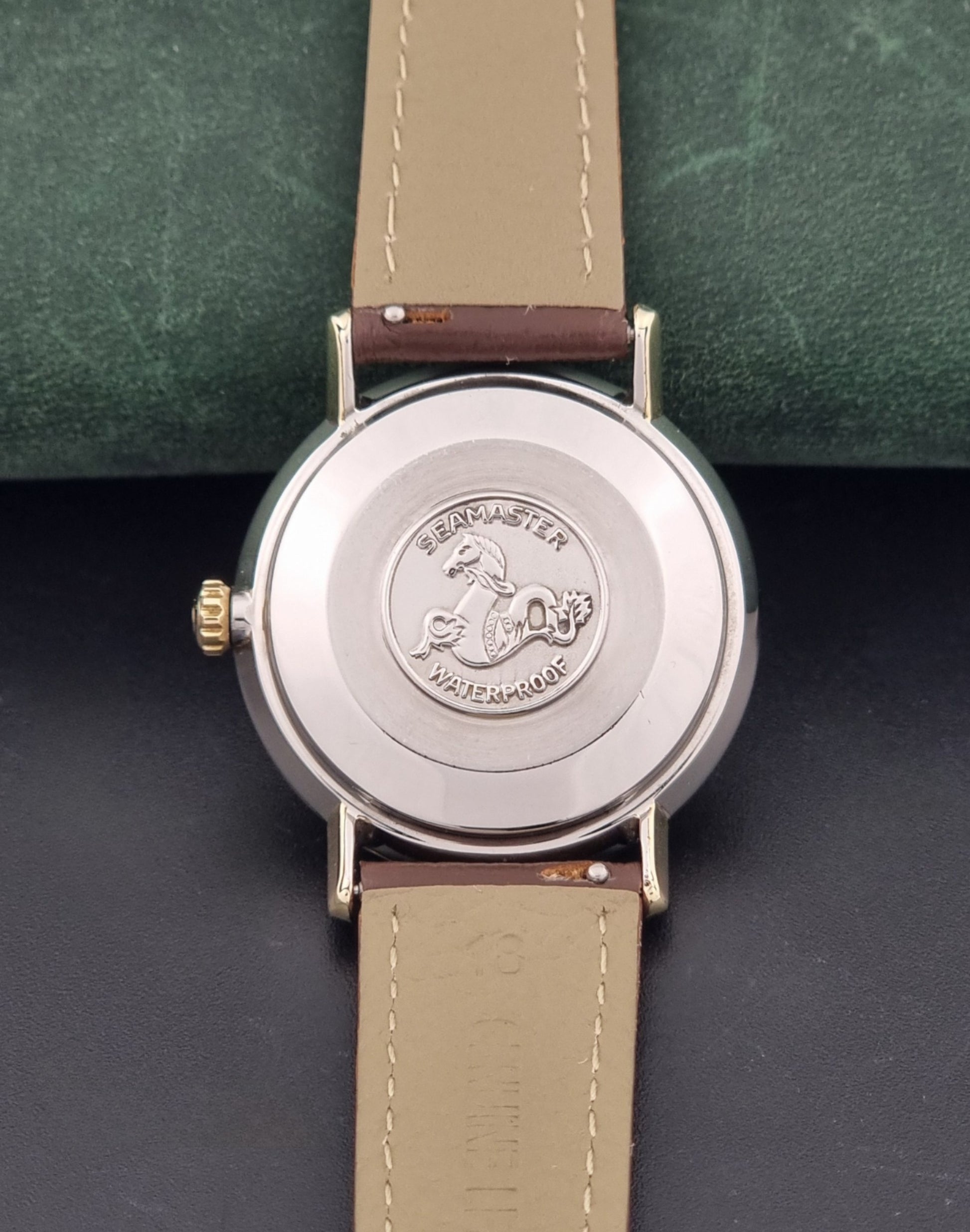 Vintage Omega Wristwatch Seamaster De-ville 166.020 with a brown textured leather strap, gold case, on a dark gray background case back view