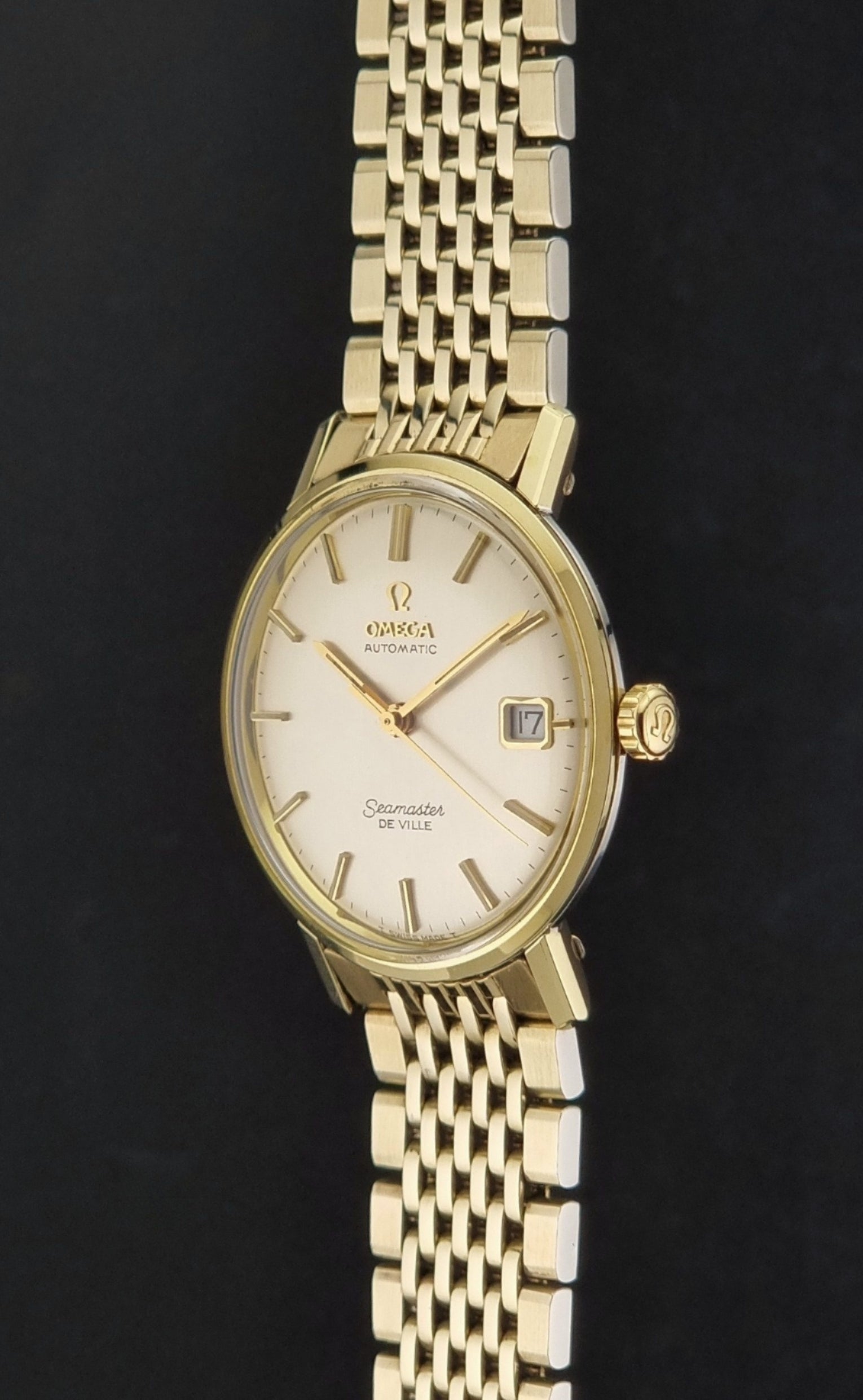Vintage Omega Wristwatch Seamaster De-ville 166.020 with gold omega bracelet, gold case, on a dark gray background crown profile view