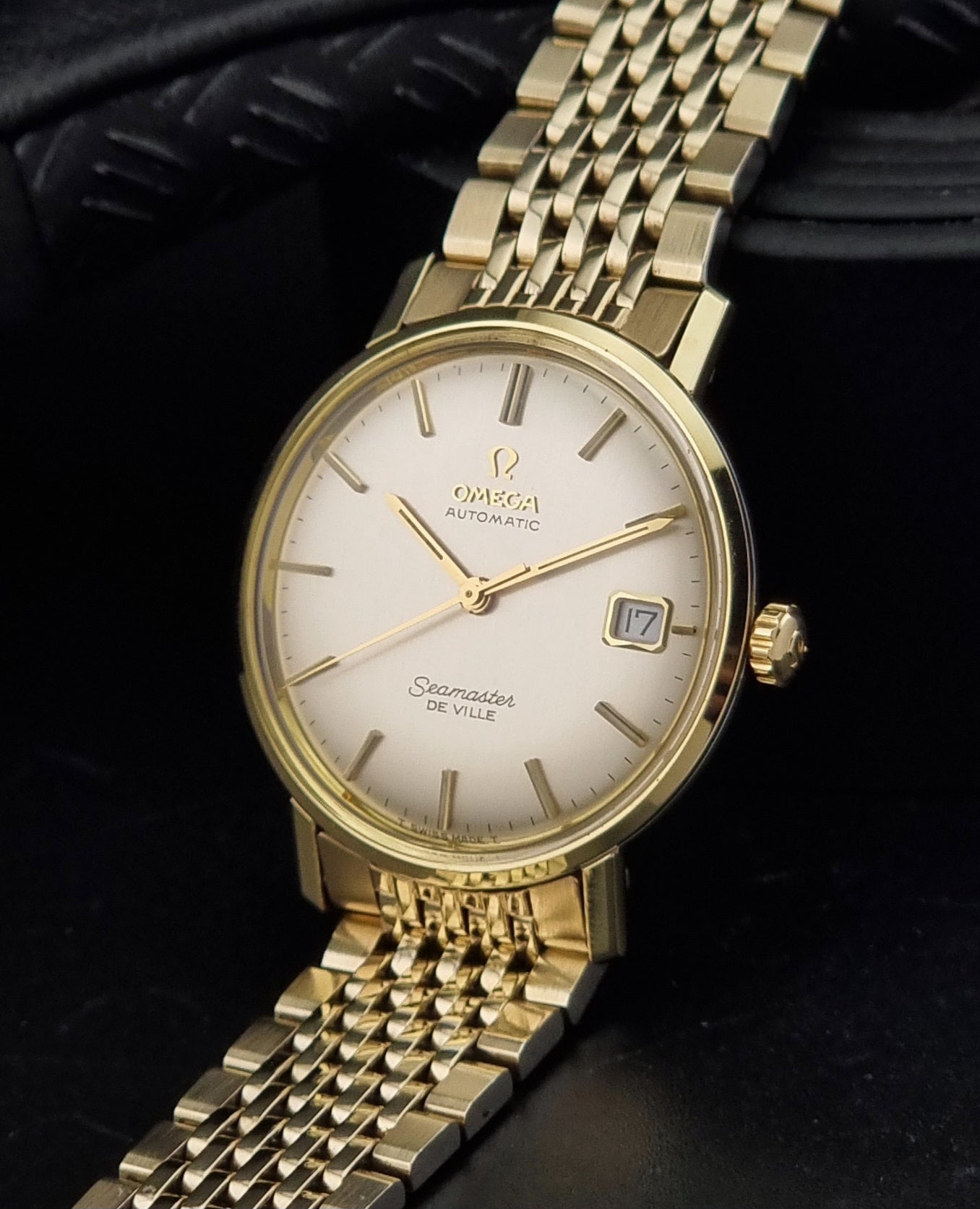 Vintage Omega Wristwatch Seamaster De-ville 166.020 with gold omega bracelet, gold case, on a dark gray background crown view