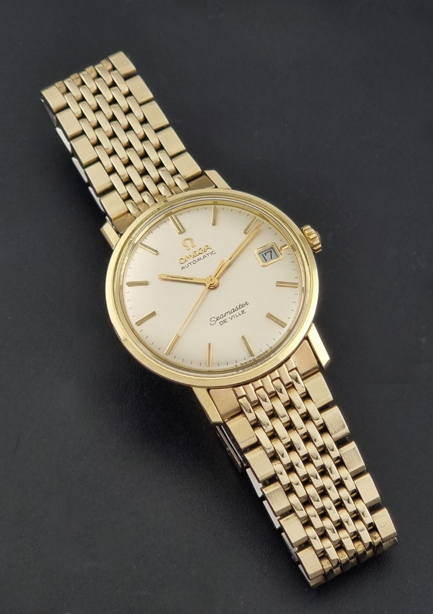 Vintage Omega Wristwatch Seamaster De-ville 166.020 with gold omega bracelet, gold case, on a dark gray background close up dial view