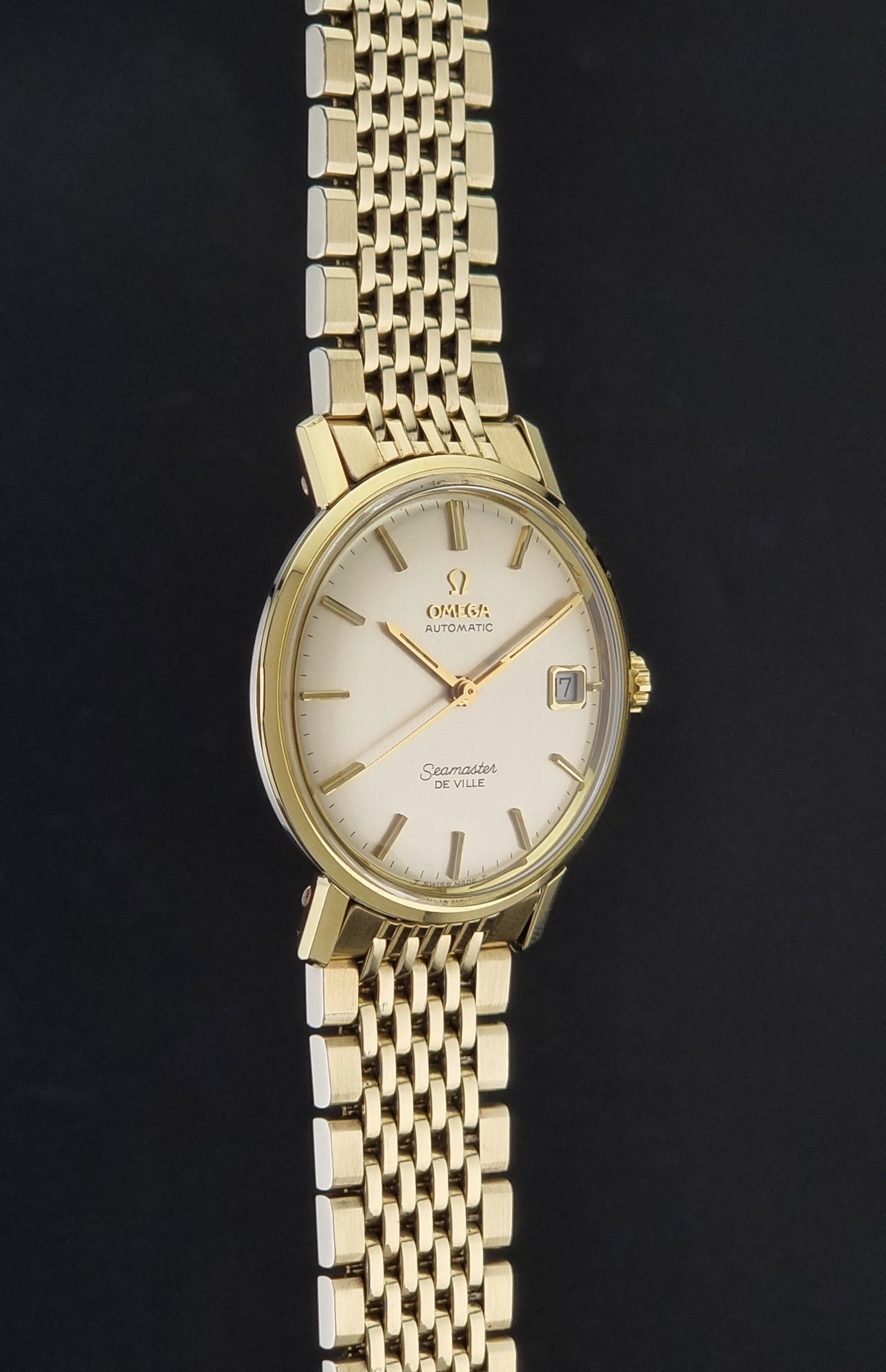 Vintage Omega Wristwatch Seamaster De-ville 166.020 with gold omega bracelet, gold case, on a dark gray background side profile view