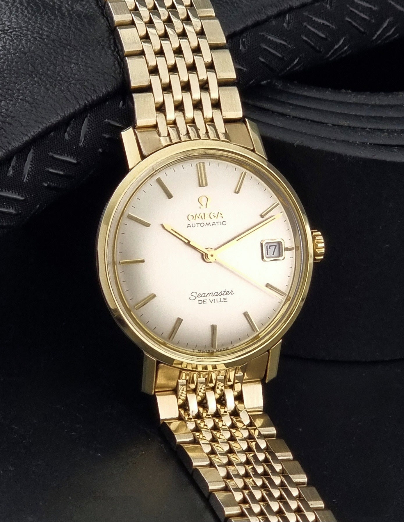 Vintage Omega Wristwatch Seamaster De-ville 166.020 with gold omega bracelet, gold case, on a dark gray background side view