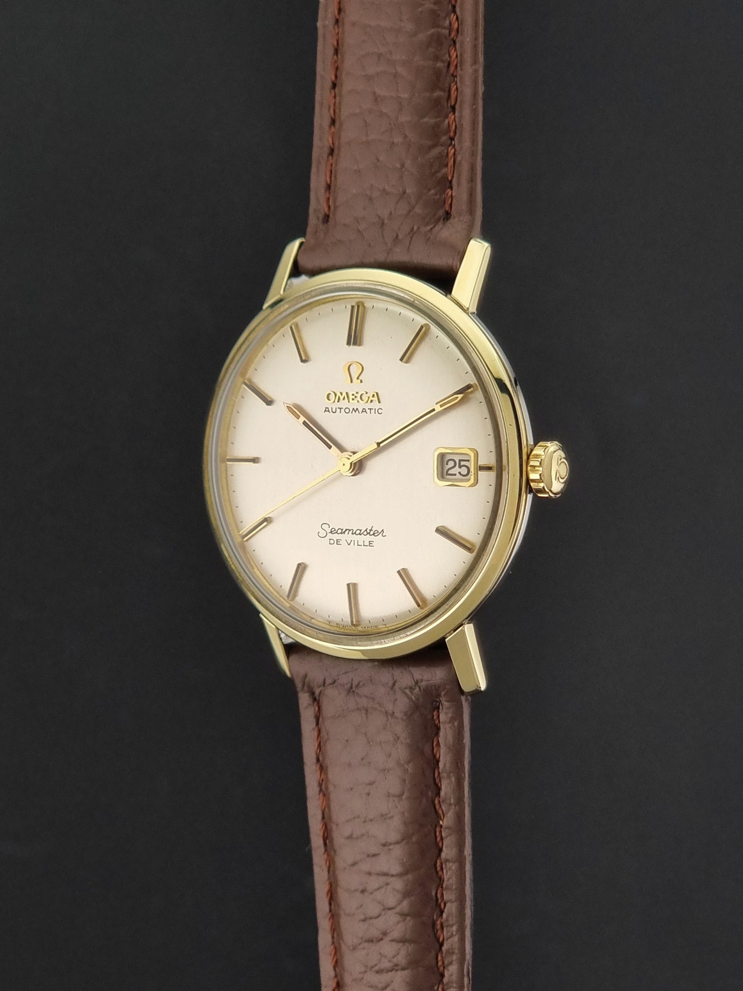 Vintage Omega Wristwatch Seamaster De-ville 166.020 with a brown textured leather strap, gold case, on a dark gray background crown profile view