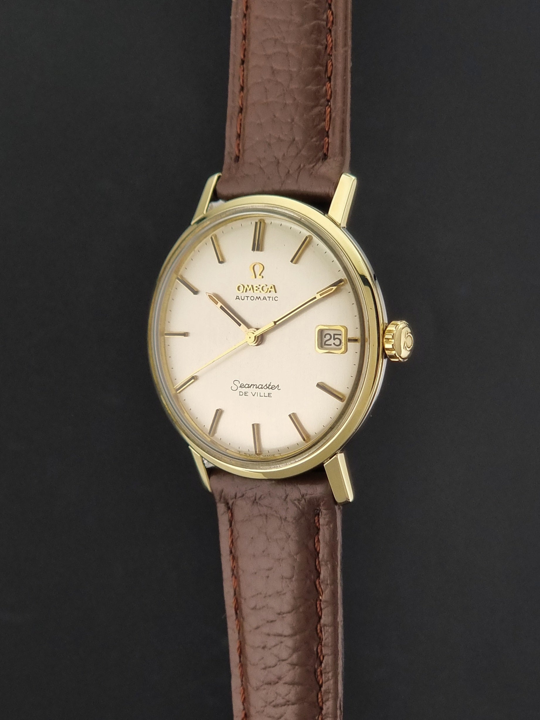Vintage Omega Wristwatch Seamaster De-ville 166.020 with a brown textured leather strap, gold case, on a dark gray background crown profile view
