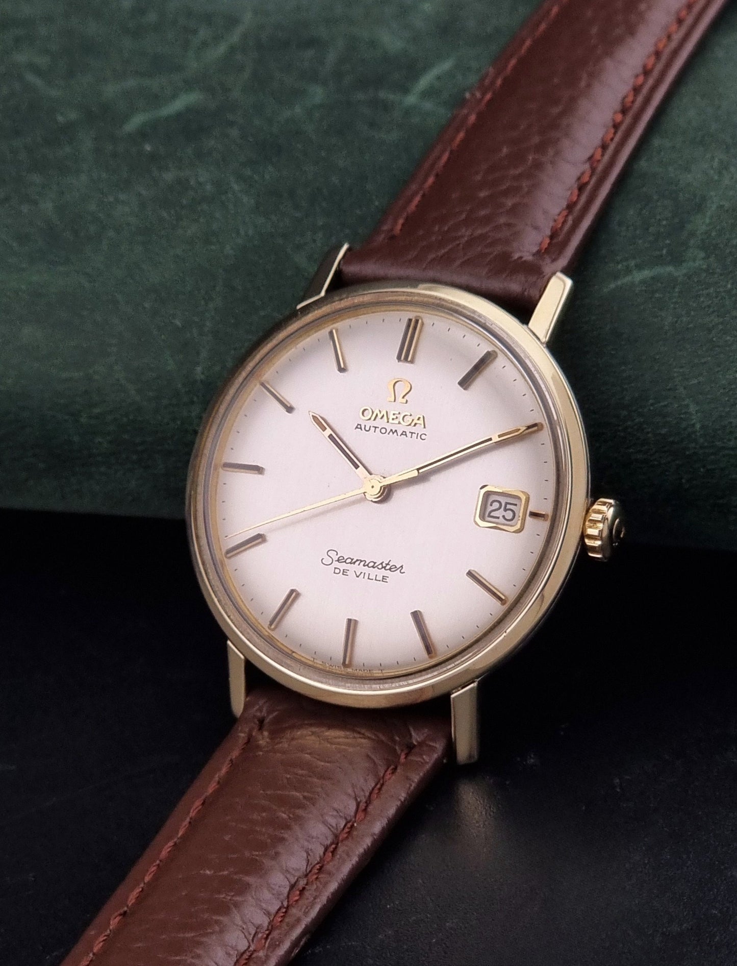 Vintage Omega Wristwatch Seamaster De-ville 166.020 with a brown textured leather strap, gold case, on a dark gray background crown view