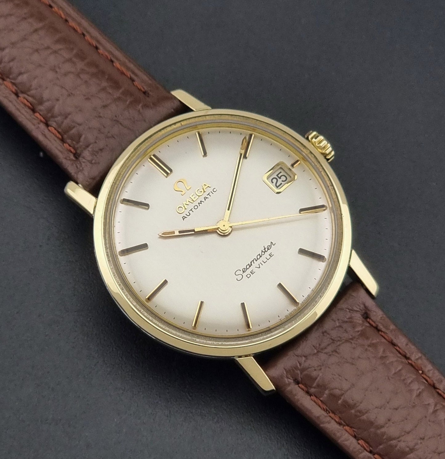 Vintage Omega Wristwatch Seamaster De-ville 166.020 with a brown textured leather strap, gold case, on a dark gray background close up dial view