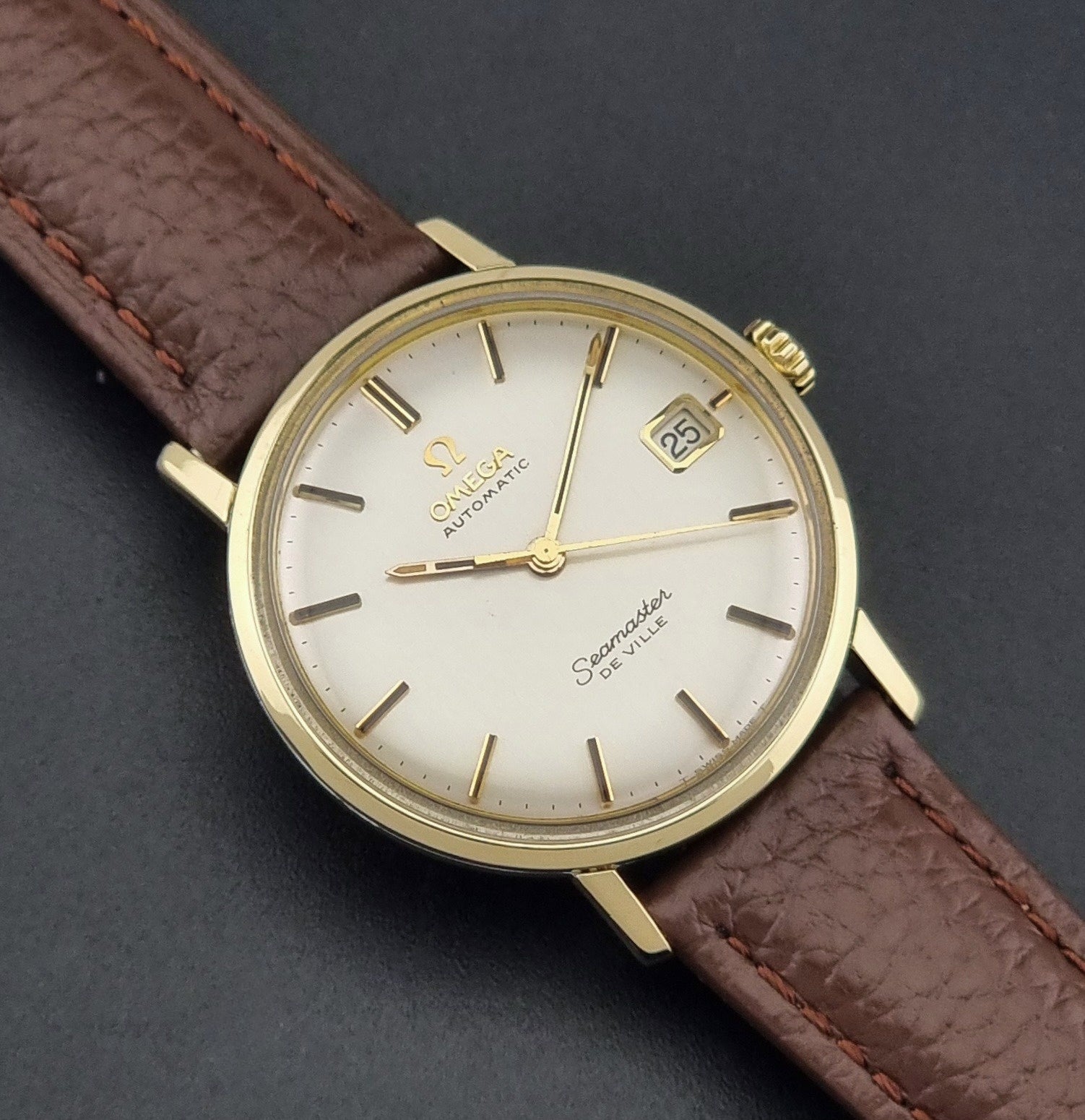 Vintage Omega Wristwatch Seamaster De-ville 166.020 with a brown textured leather strap, gold case, on a dark gray background close up dial view