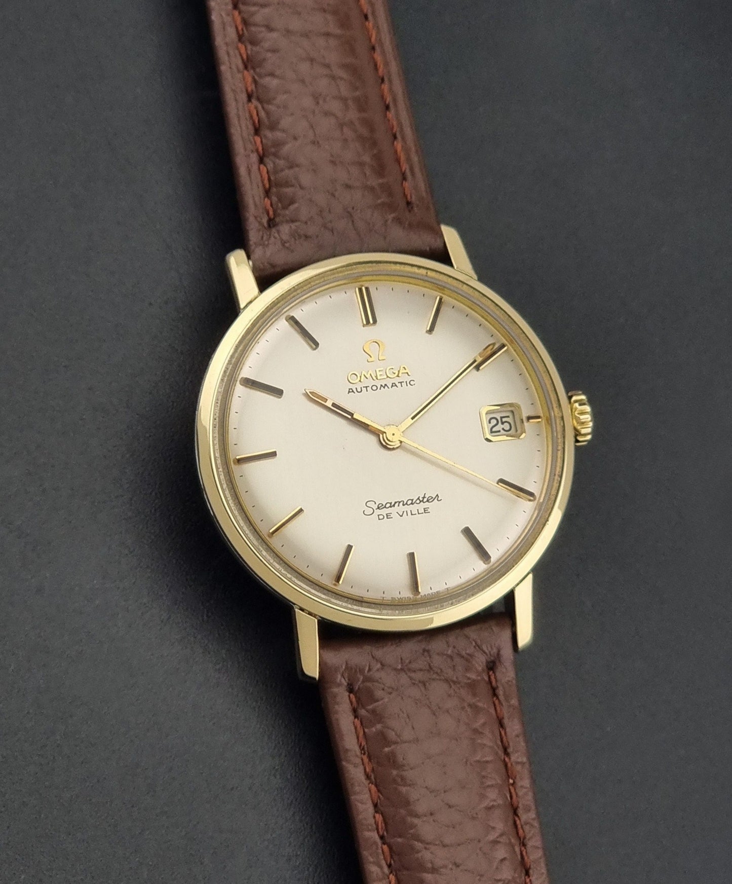 Vintage Omega Wristwatch Seamaster De-ville 166.020 with a brown textured leather strap, gold case, on a dark gray background dial view