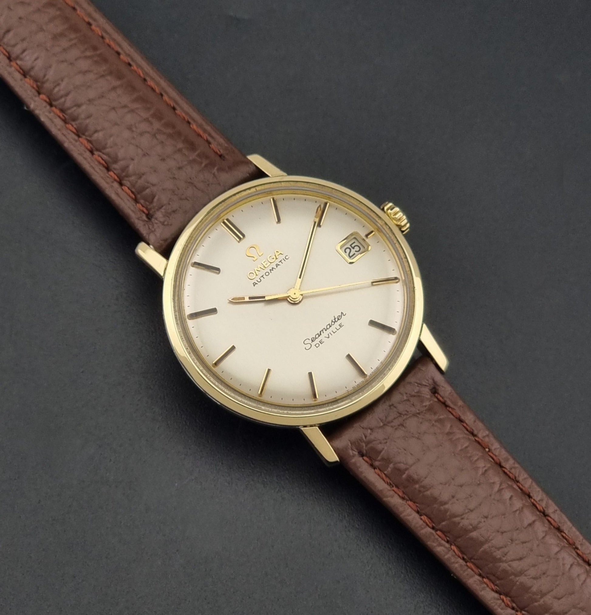 Vintage Omega Wristwatch Seamaster De-ville 166.020 with a brown textured leather strap, gold case, on a dark gray background dial