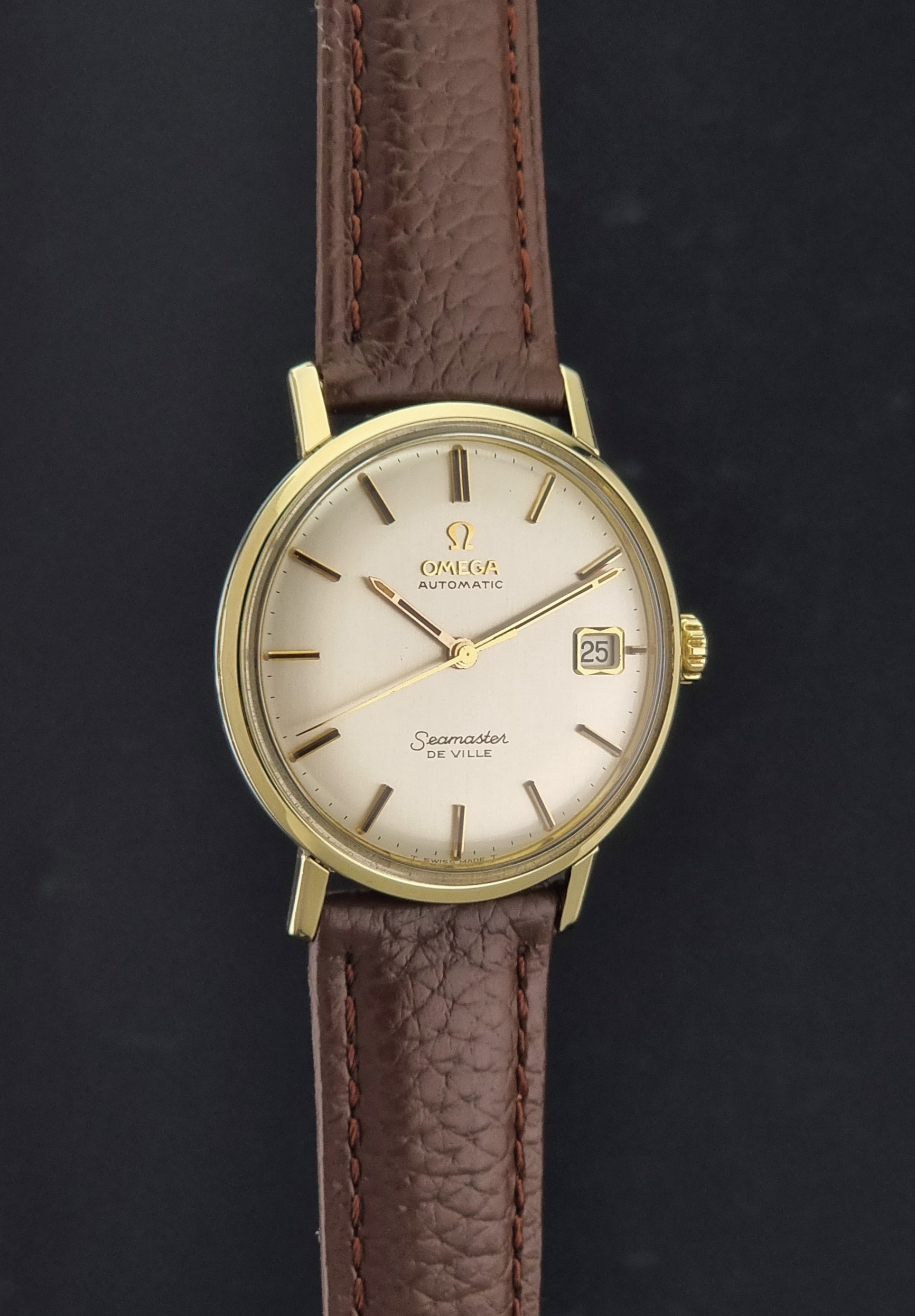Vintage Omega Wristwatch Seamaster De-ville 166.020 with a brown textured leather strap, gold case, on a dark gray background side profile view