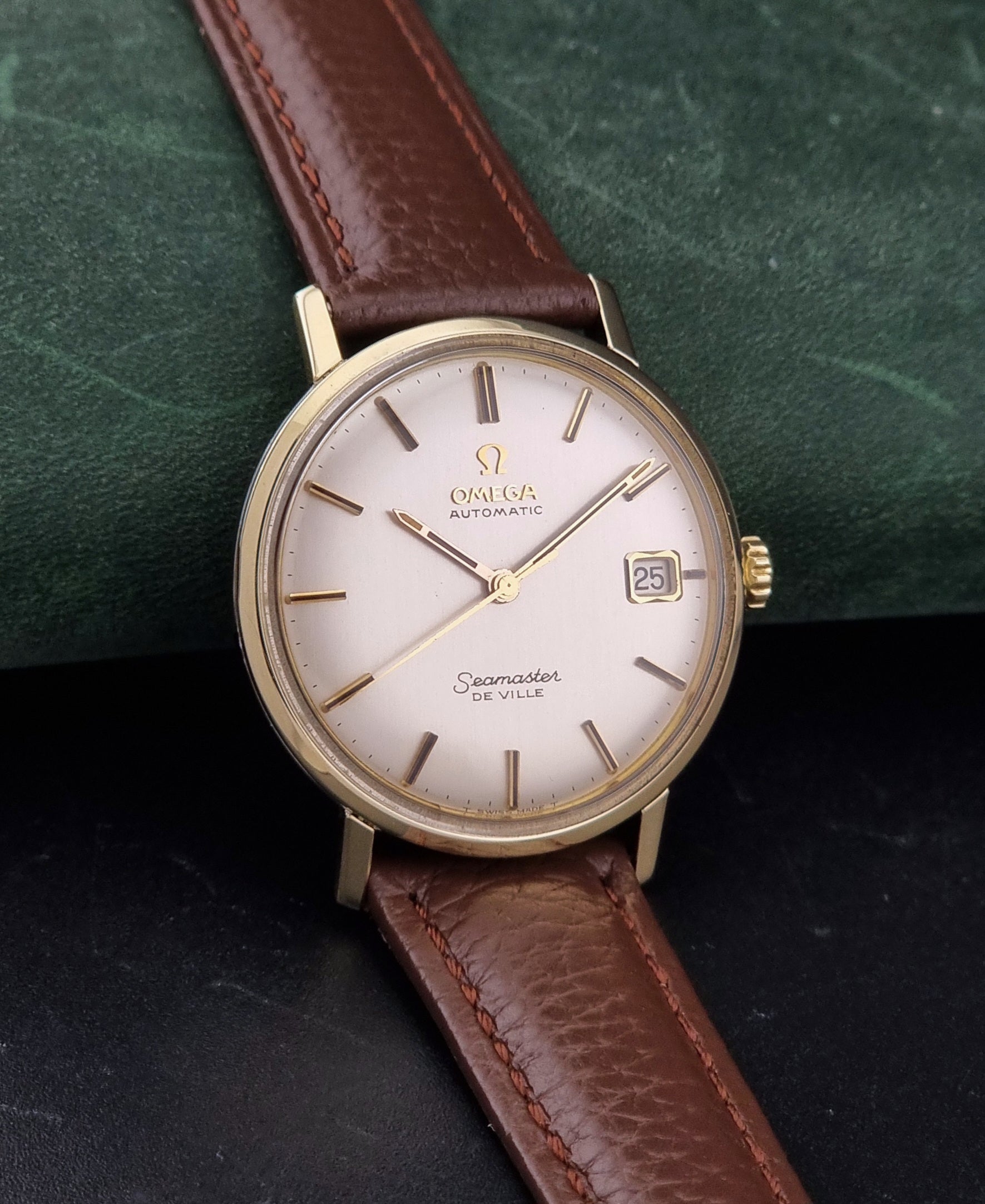 Vintage Omega Wristwatch Seamaster De-ville 166.020 with a brown textured leather strap, gold case, on a dark gray background side view