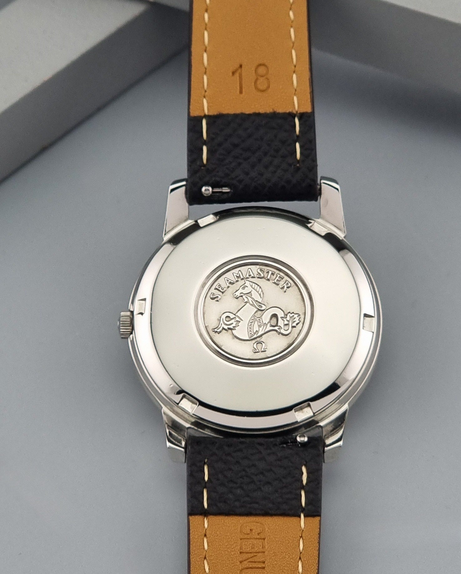Vintage Omega Wristwatch Seamaster 165.003 with a silver-toned round case and black textured strap, shown on a gray background case back view