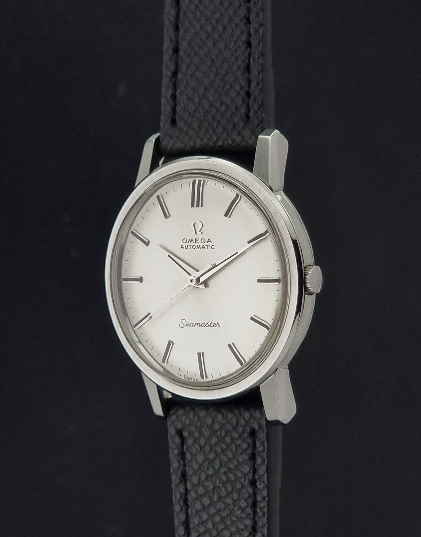Vintage Omega Wristwatch Seamaster 165.003 with a silver-toned round case and black textured strap, shown on a gray background crown profile view